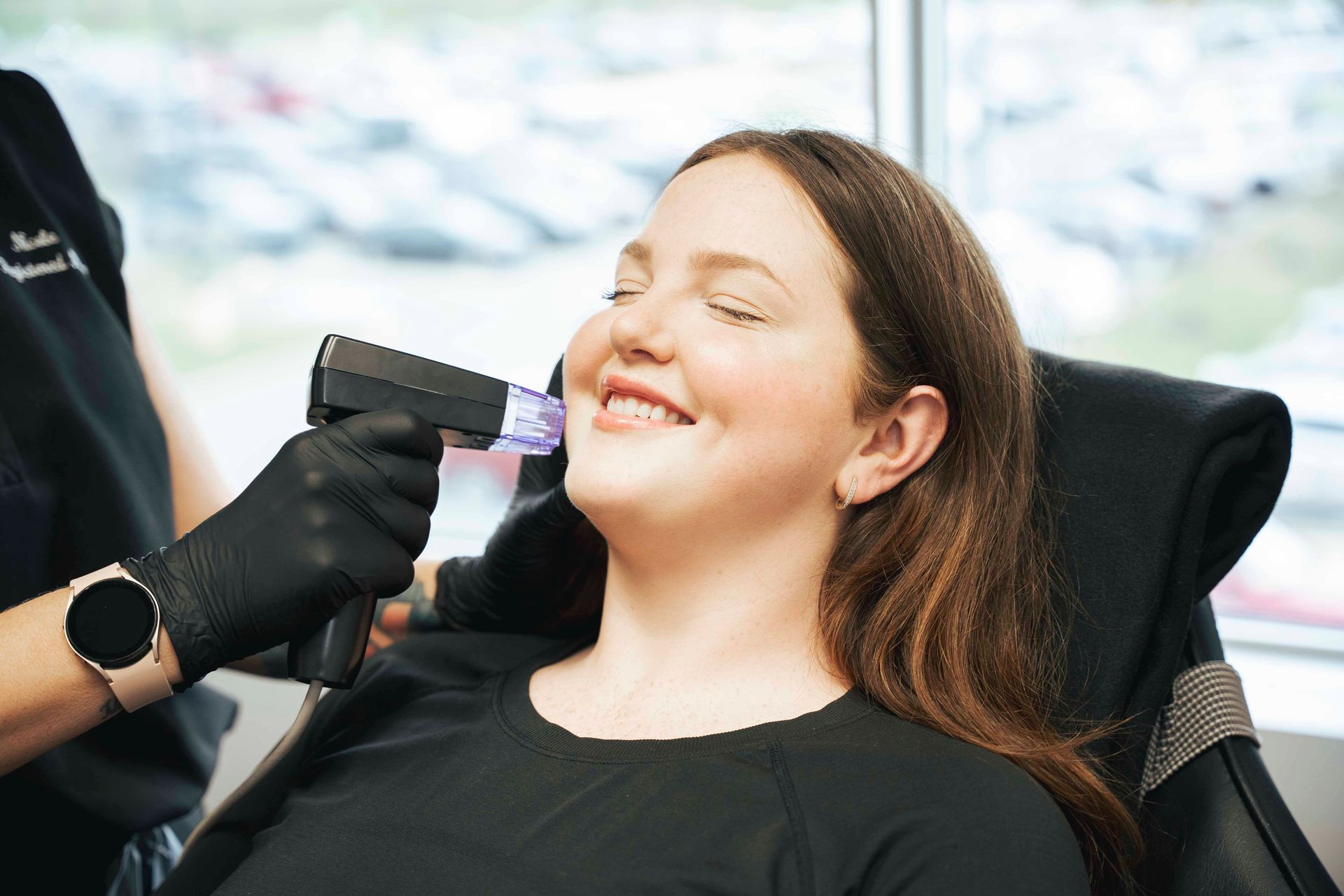 Woman receiving facial microneedling treatment, smiling with eyes closed; in a clinic.