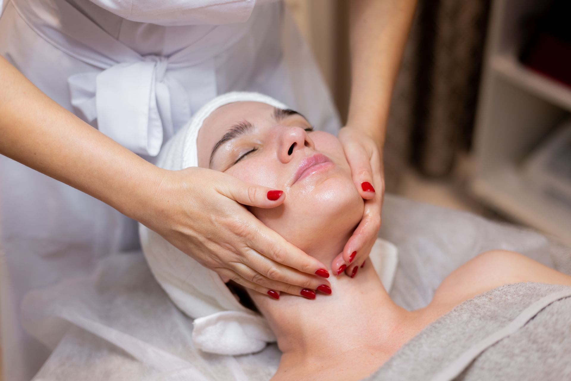 Woman receiving a facial treatment, with hands on her face and neck in a spa setting.