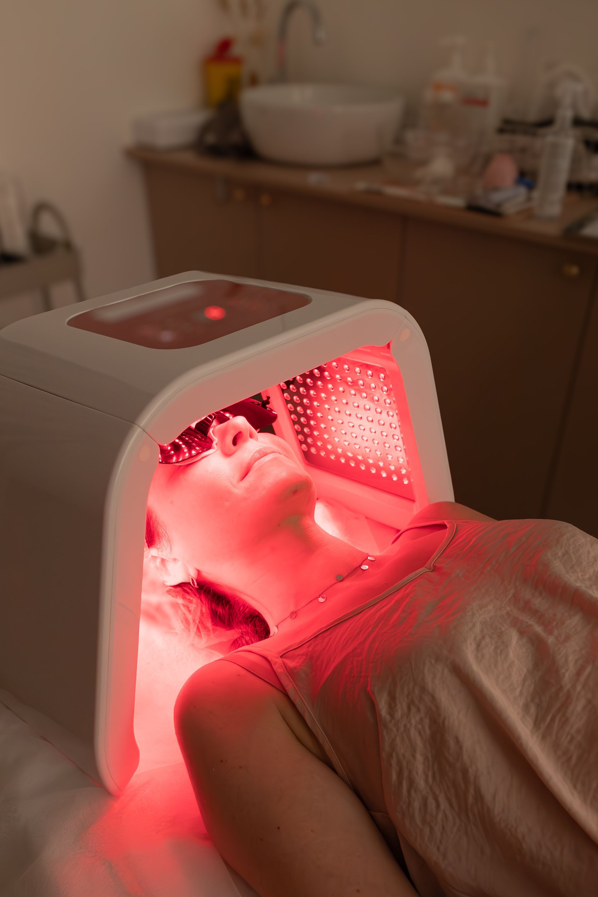 Woman receiving red light therapy facial treatment at a clinic.