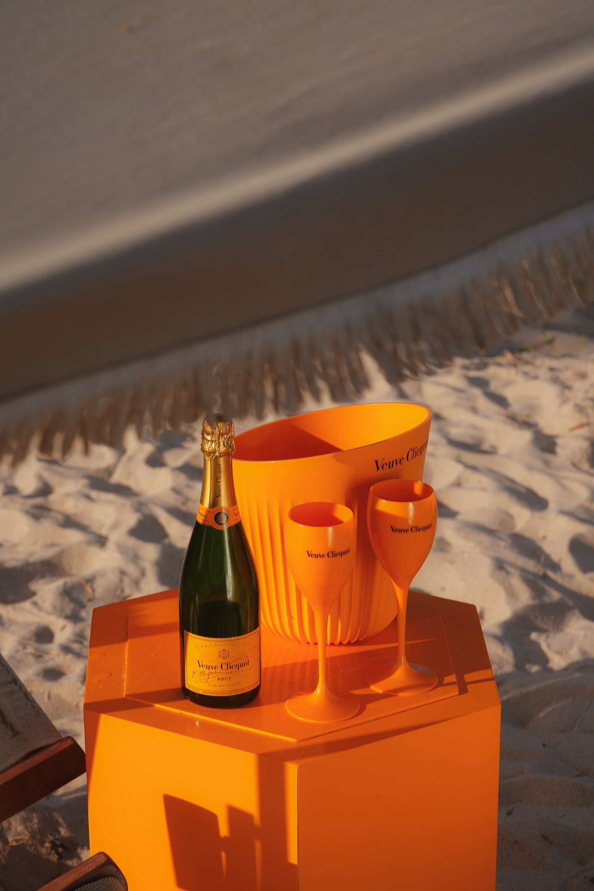 Uma garrafa de champanhe e duas taças estão sobre uma mesa na praia.