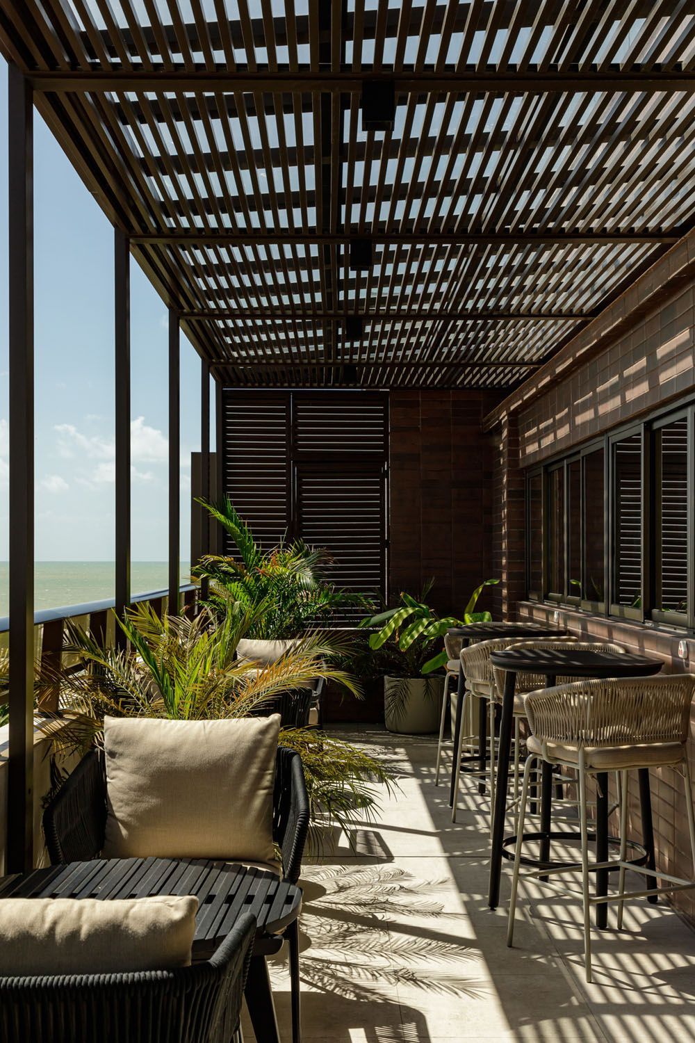 Uma varanda com pérgola, cadeiras, mesas e plantas.