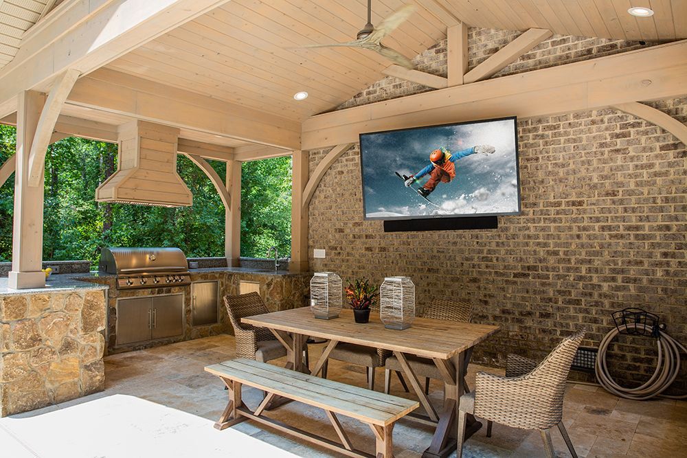A large flat screen tv is mounted on a brick wall above a picnic table.