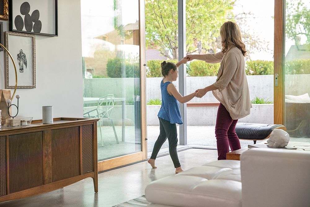 A woman and a little girl are dancing in a living room.