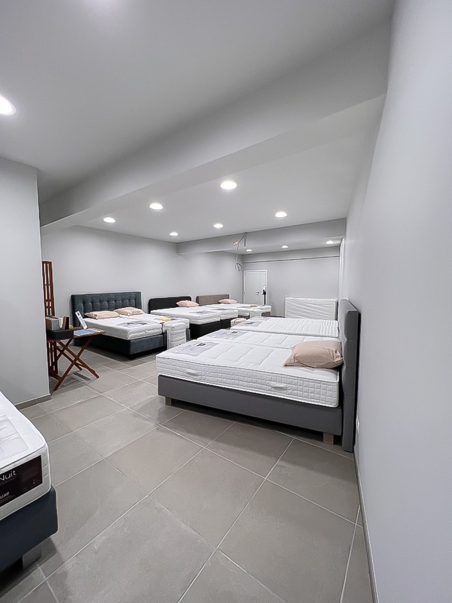 Interieur van een slaapkamermeubelwinkel, met bedden in verschillende maten. Kleurenschema grijs en wit.