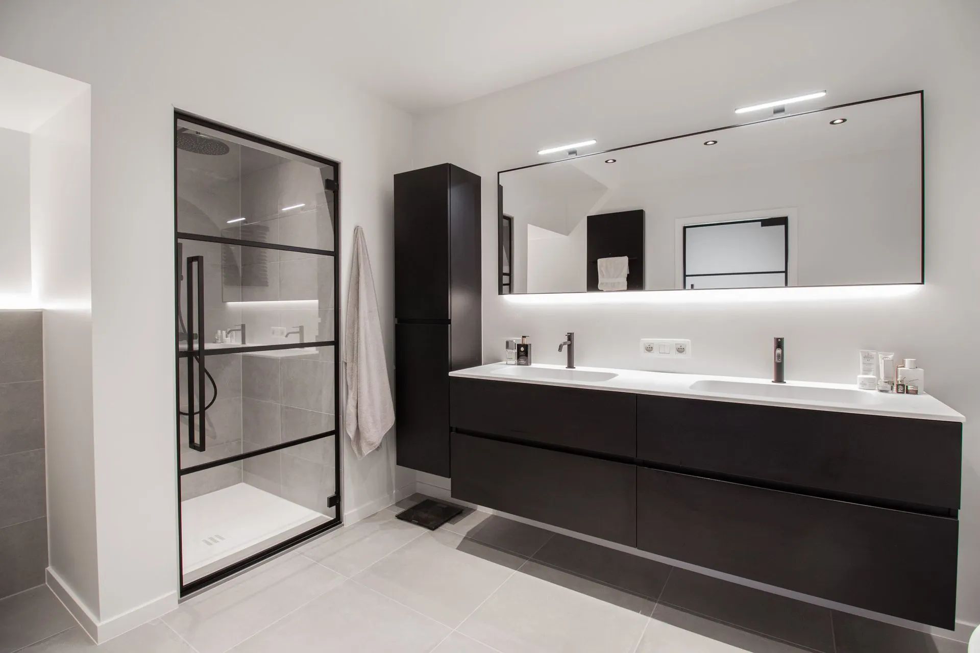 Moderne badkamer met zwarte wastafel, dubbele wastafels en glazen douche met inbouwverlichting.