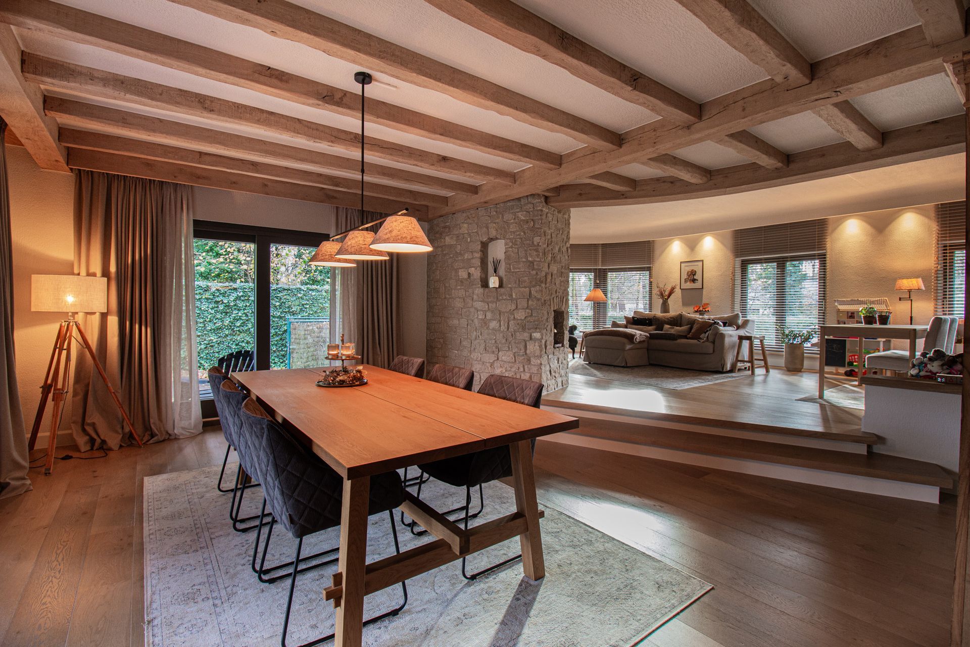 Eetkamer met houten tafel, stoelen en open zicht op de woonkamer met bank.