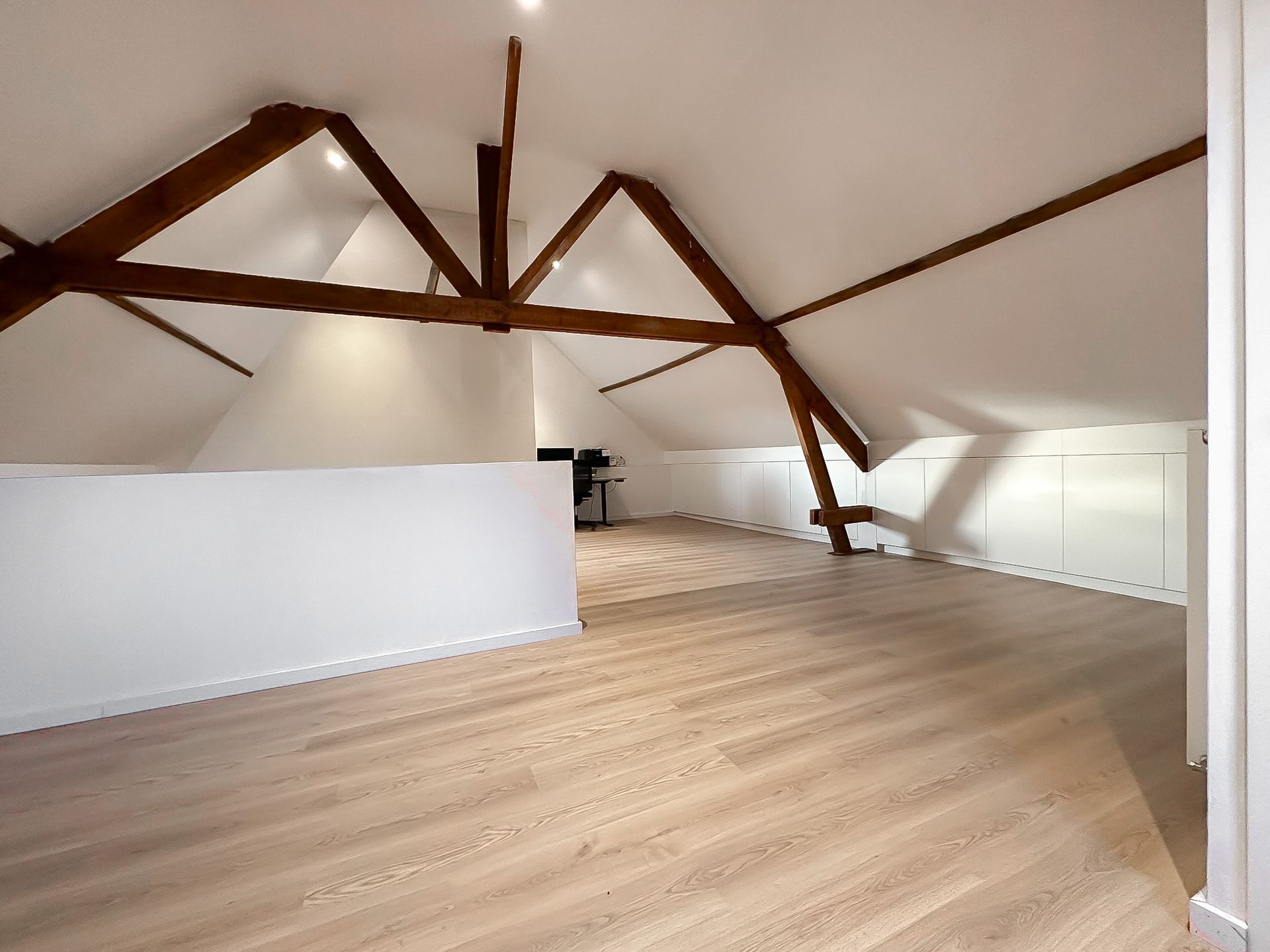 Ruime zolderkamer met houten balken, schuin wit plafond en lichte vloer met houtlook.
