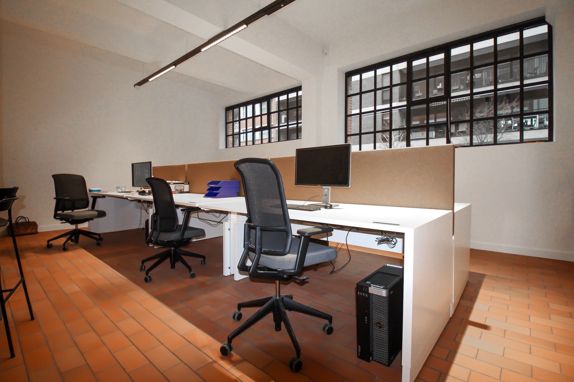Kantoorruimte met bureaus, stoelen, computers en ramen. Houten vloer, witte muren en neutrale scheidingswanden.