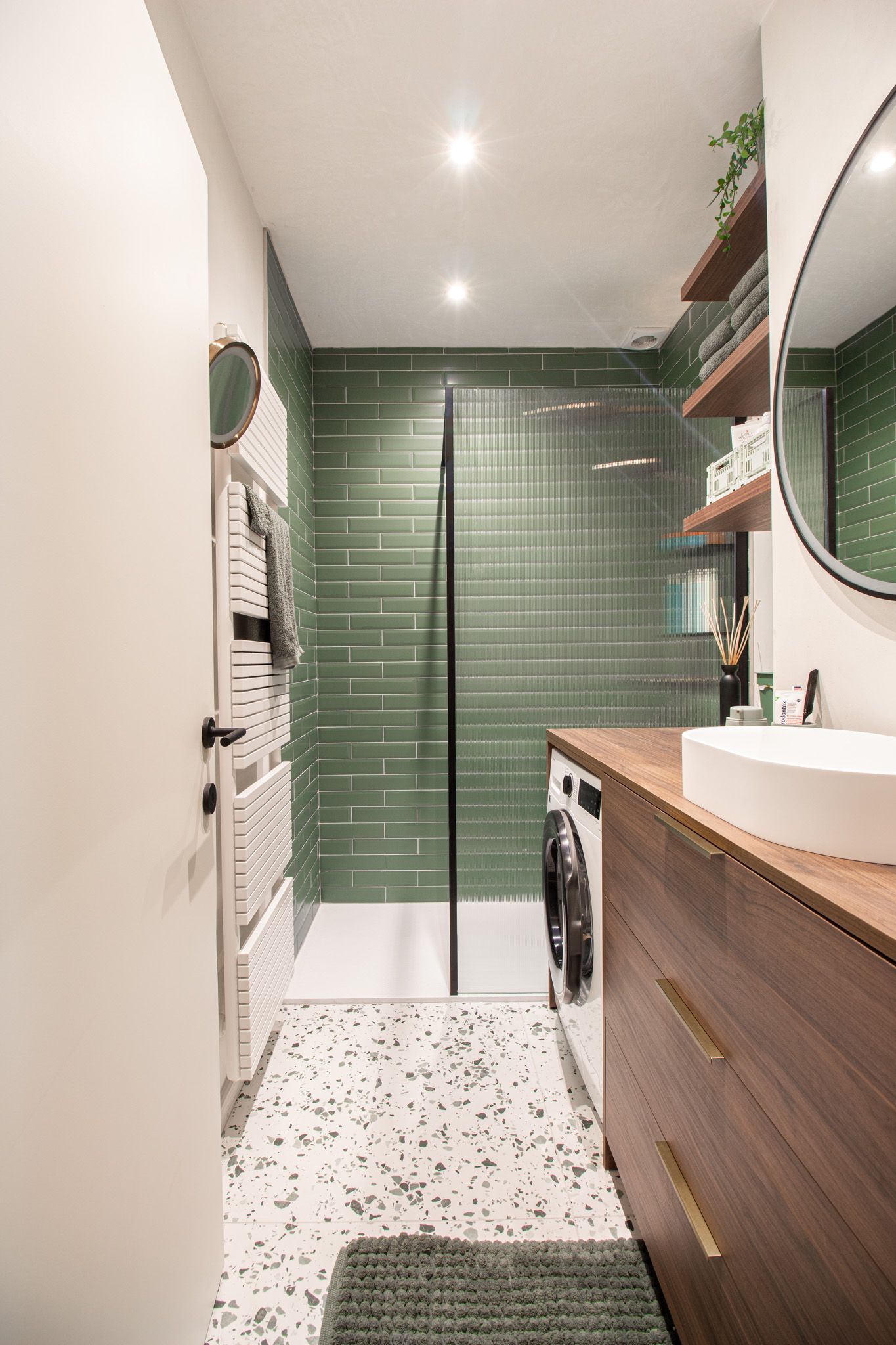 Kleine badkamer met groene tegeldouche, houten wastafel en terrazzovloer.