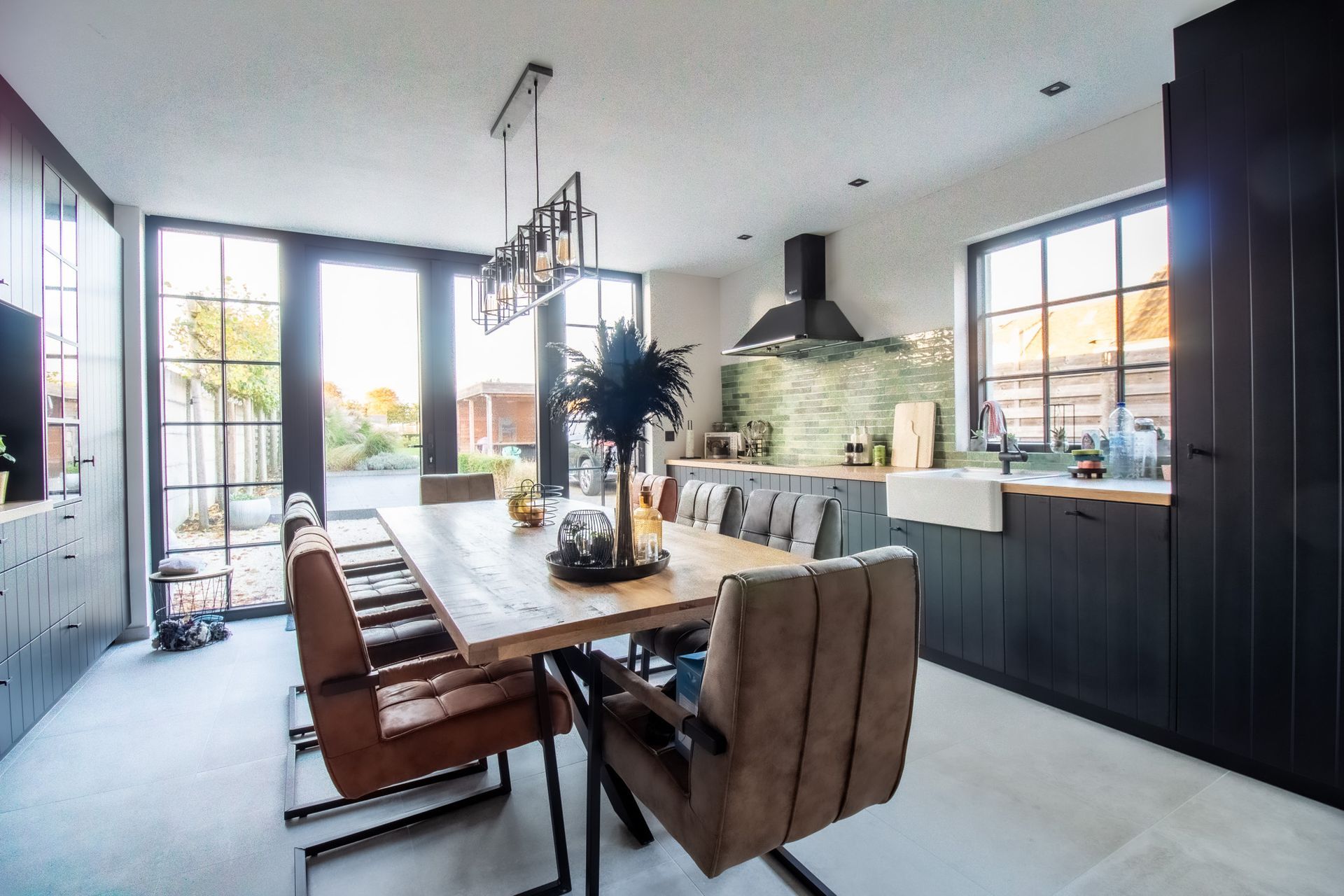 Eetkamer: lange houten tafel met leren stoelen, donkere kasten, grote ramen, modern design.