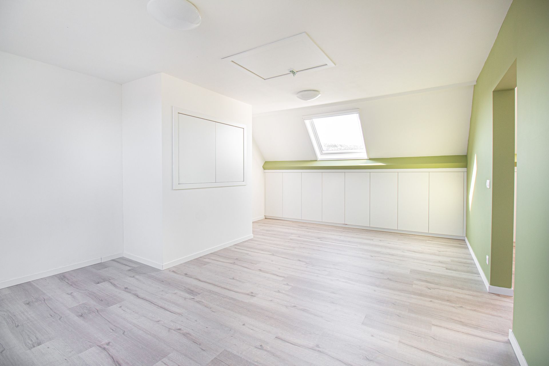 Lege kamer met witte muren, een lichte houten vloer, een dakraam en ingebouwde kasten.