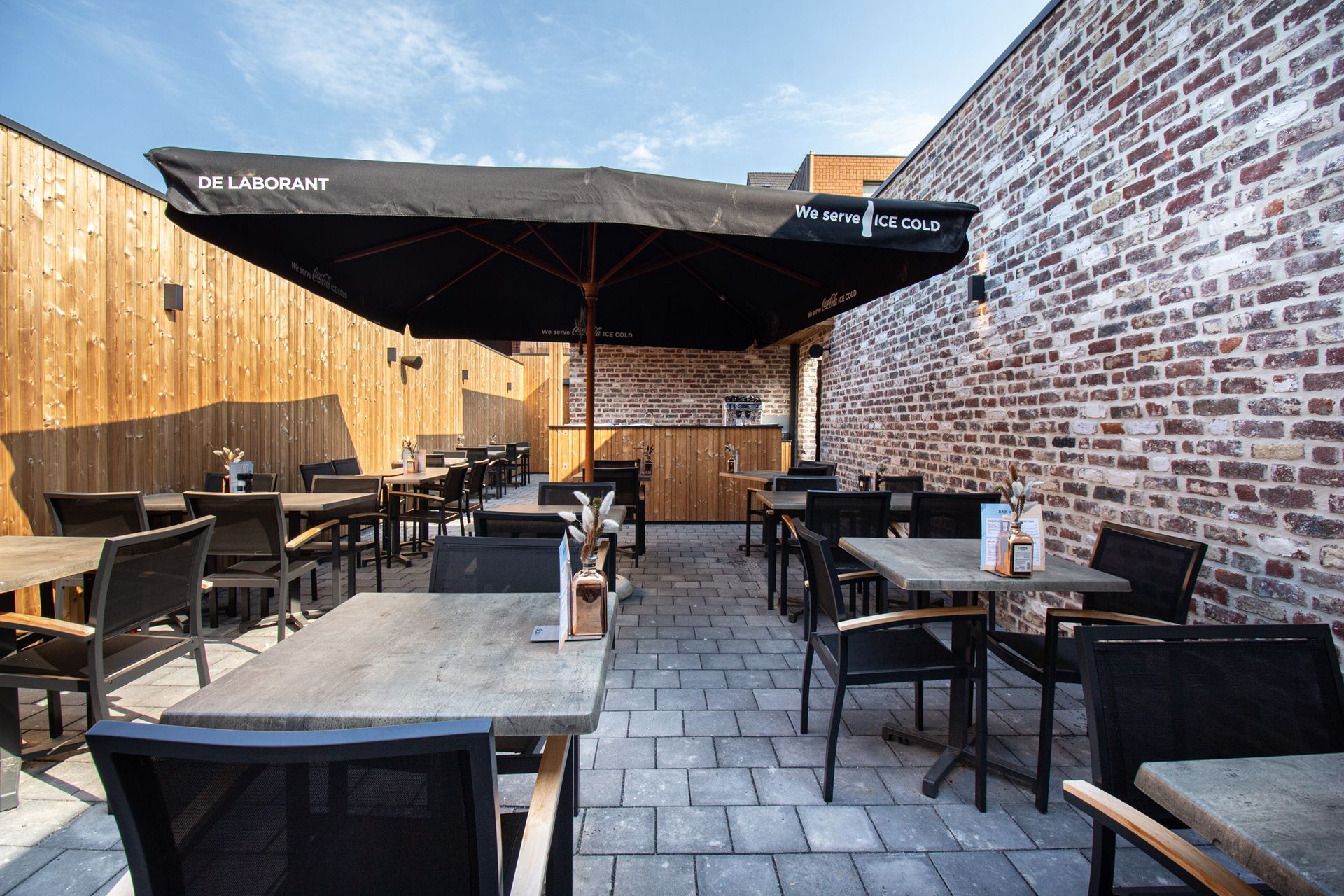 Buitenterras met tafels en stoelen, bakstenen muur, houten muur en een grote parasol.