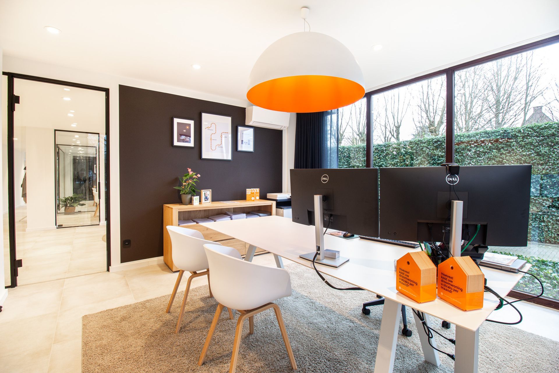 Modern kantoor met wit bureau, drie beeldschermen en een groot raam met uitzicht op het groen.