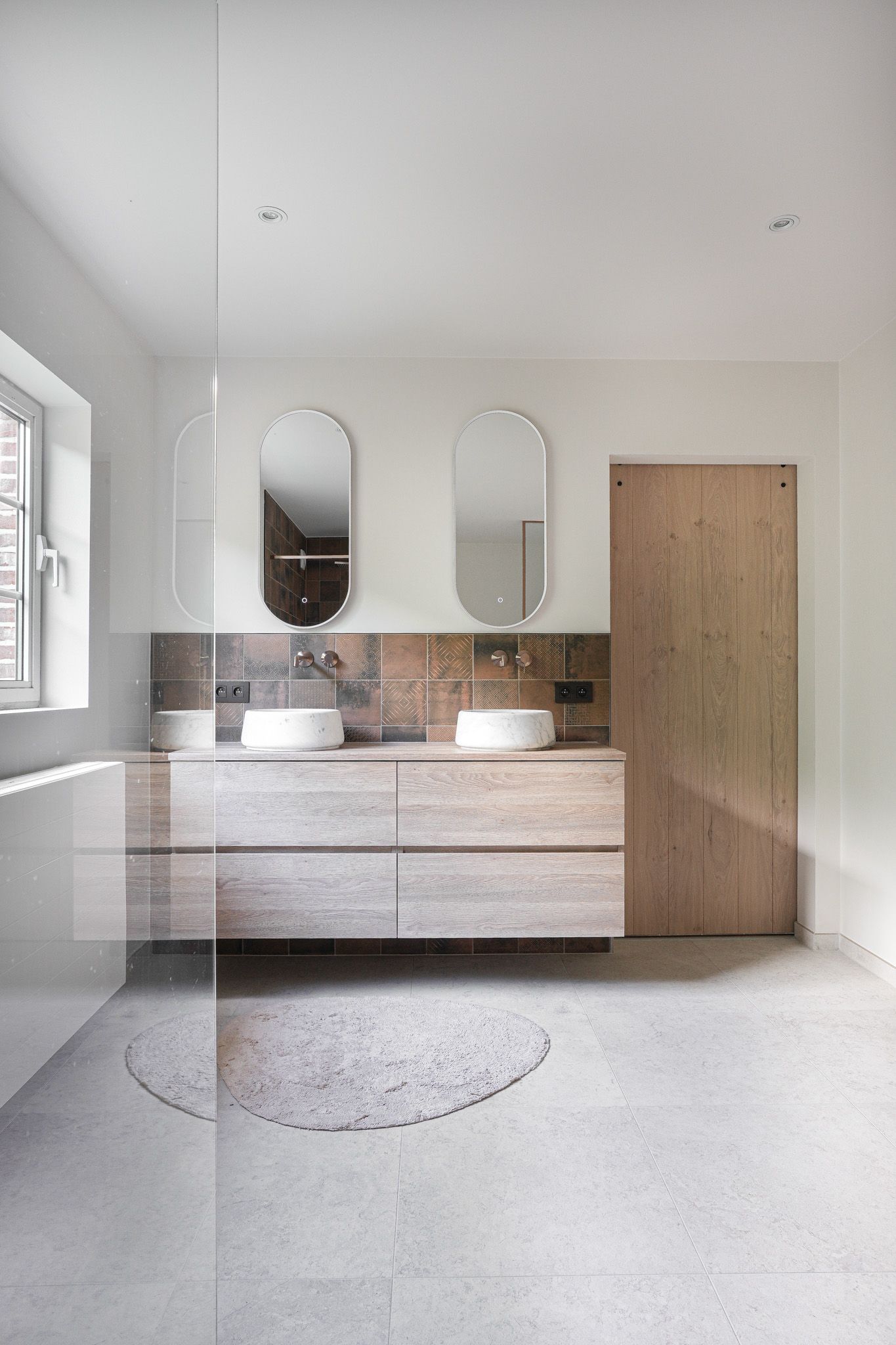 Moderne badkamer met dubbele wastafel, ovale spiegels en houten deur.