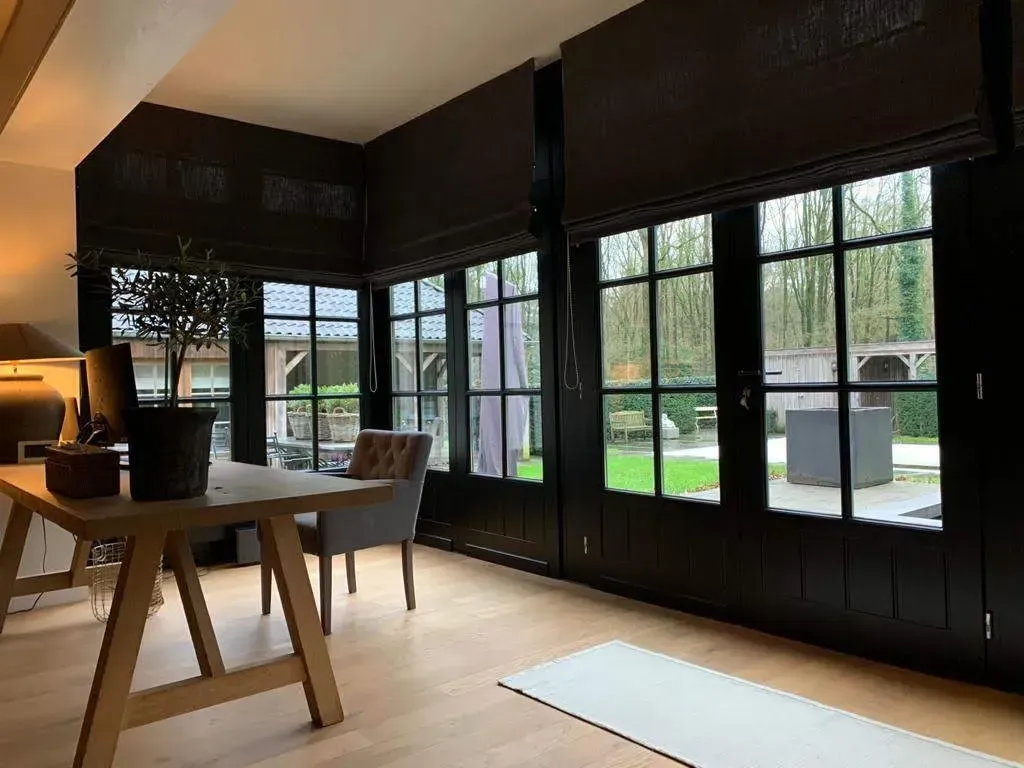 Thuiskantoor met donkere kozijnen, houten bureau, grijze stoel en uitzicht op de achtertuin.