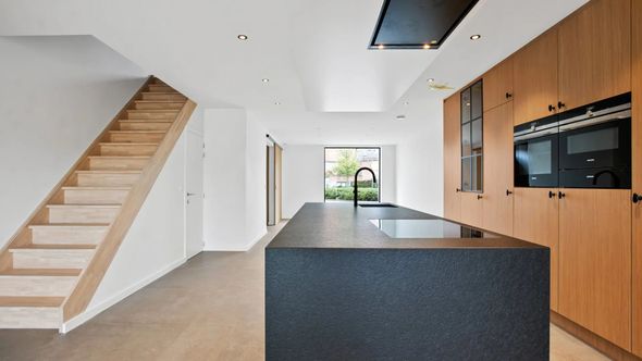 Moderne keuken met houten kasten, zwart kookeiland en trap.