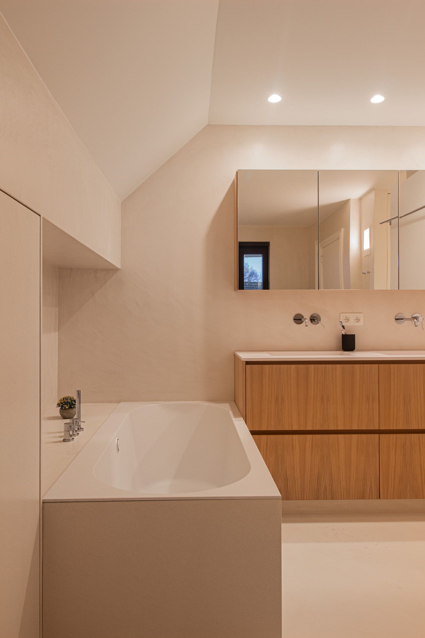 Moderne badkamer met een wit bad, houten wastafel en grote spiegel.