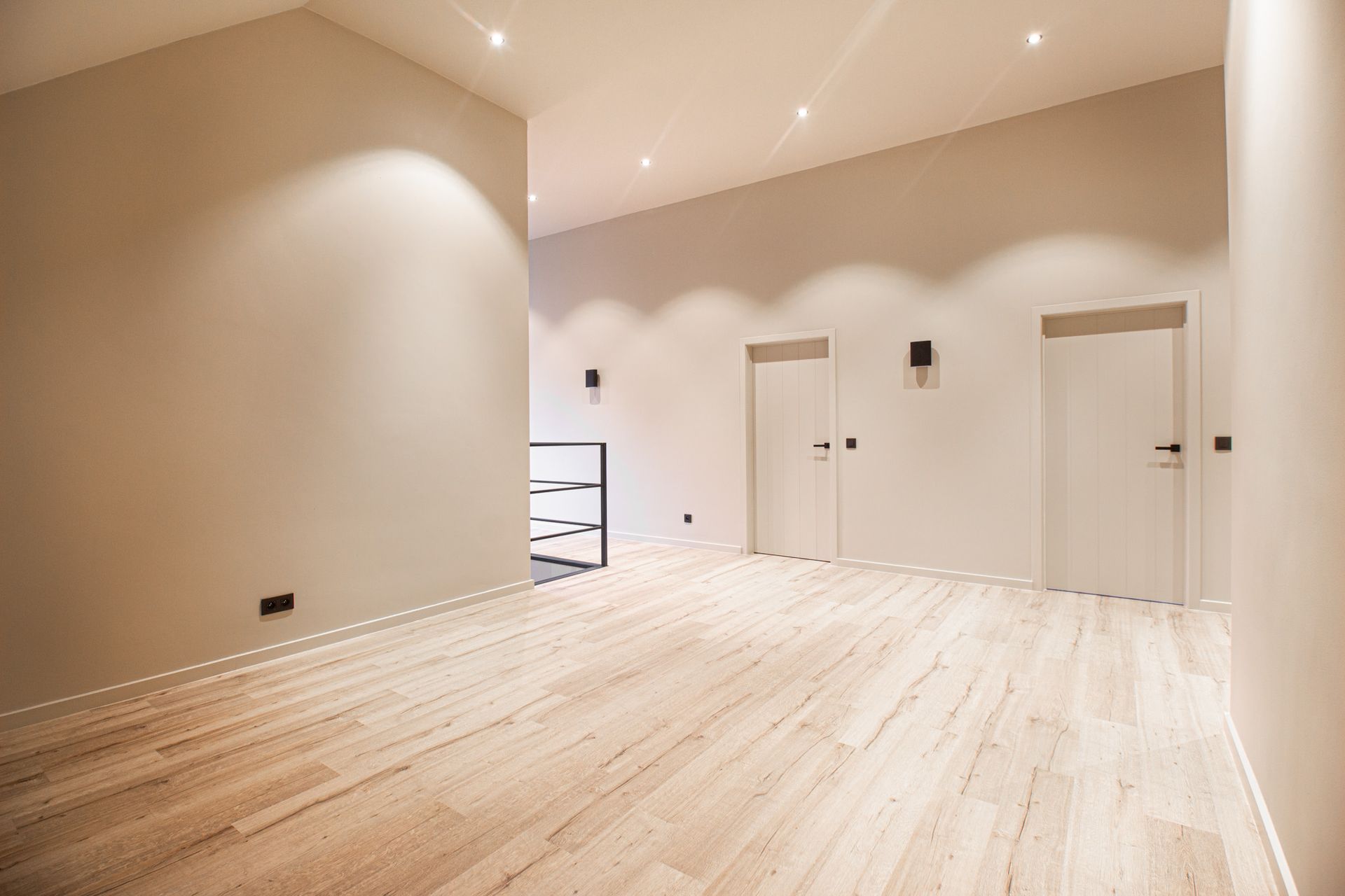 Lege kamer met lichte houten vloer, beige muren en twee witte deuren.