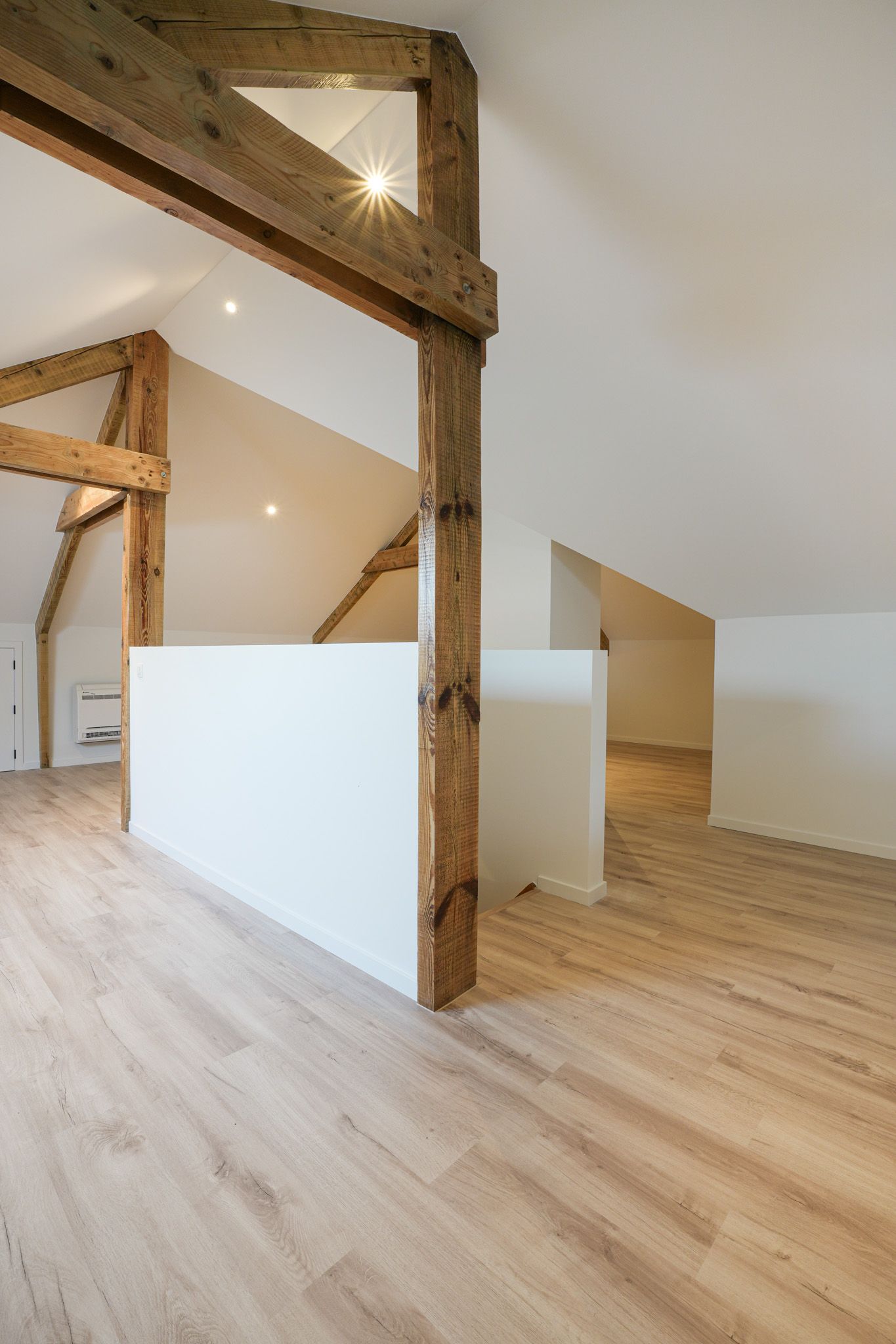 Lichte, luchtige loftruimte met lichte houten vloeren, witte muren en zichtbare houten balken.