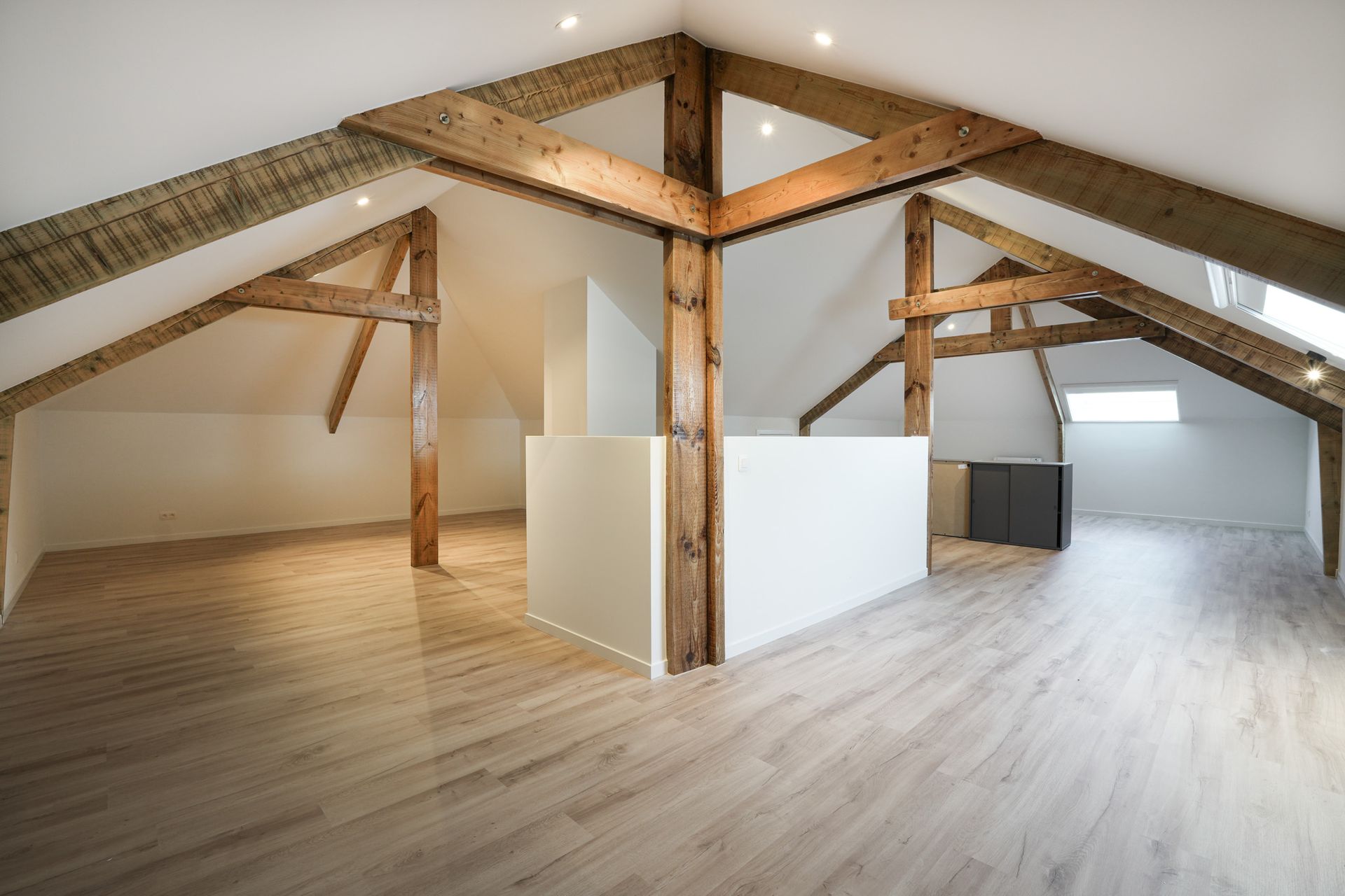Open zolder met zichtbare houten balken, witte muren en lichte houten vloer.