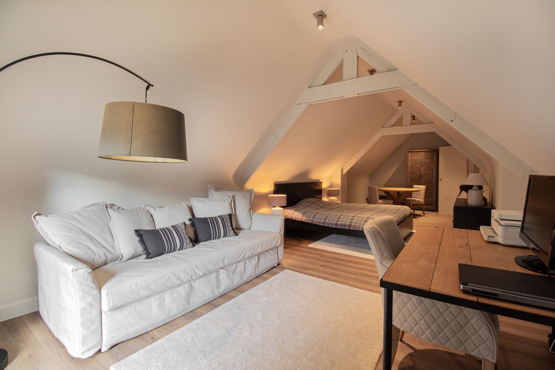Gezellige zolderkamer met witte bank, bed en bureau onder schuin plafond.