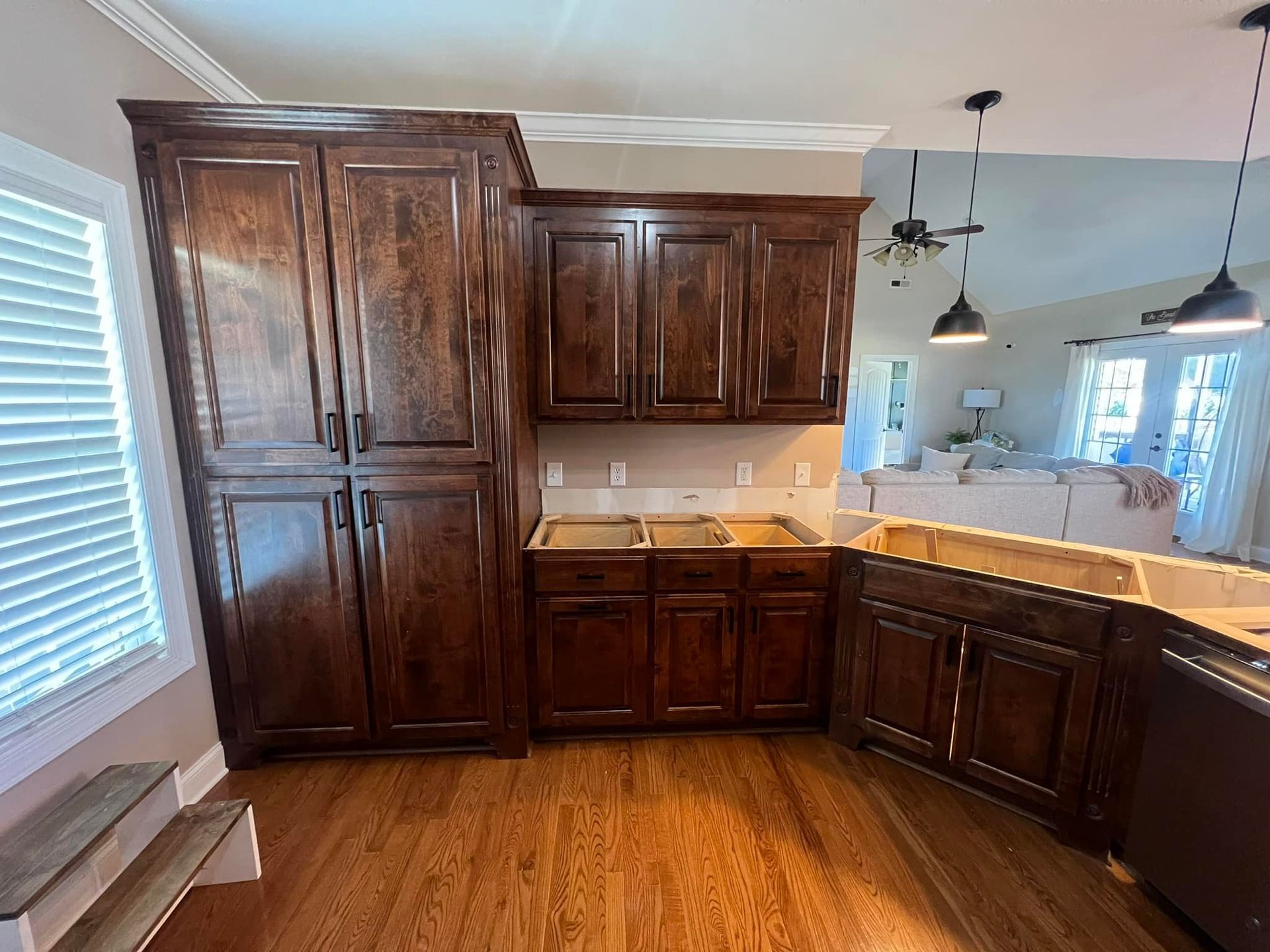 A kitchen area with dark wood cabinets, a tall pantry, and an open layout view into a living room with pendant lighting.