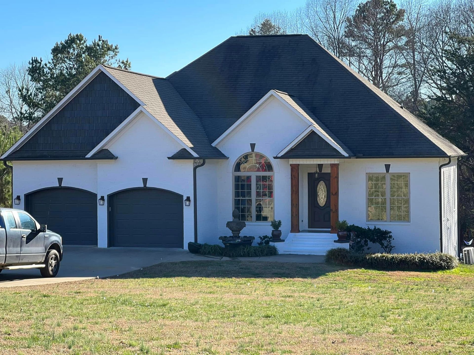A white house with a dark roof and a two-car garage, with a gray truck parked in the driveway and a grassy lawn in front.