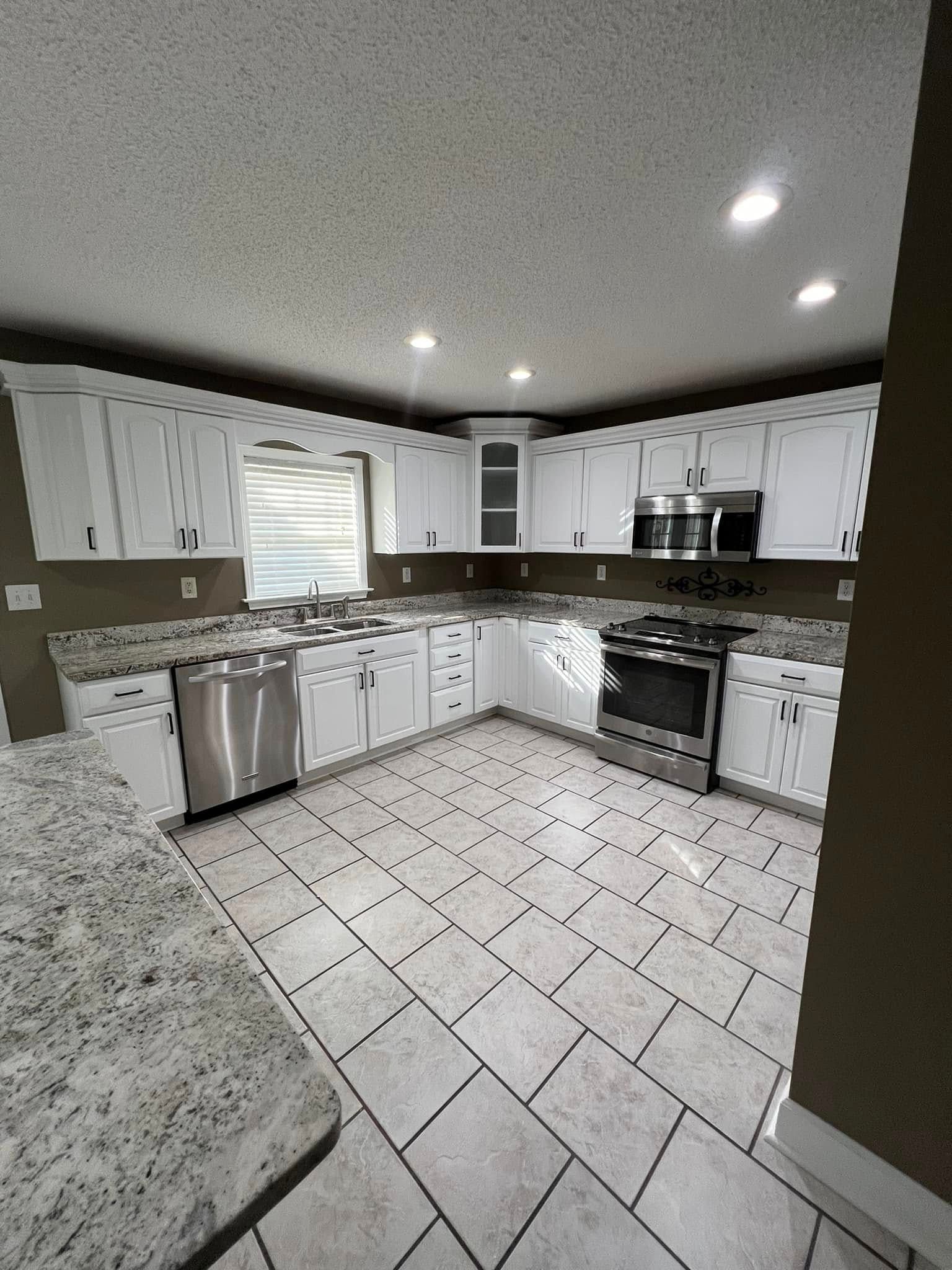 A bright kitchen with white cabinets, speckled granite countertops, stainless steel appliances, and tiled flooring.