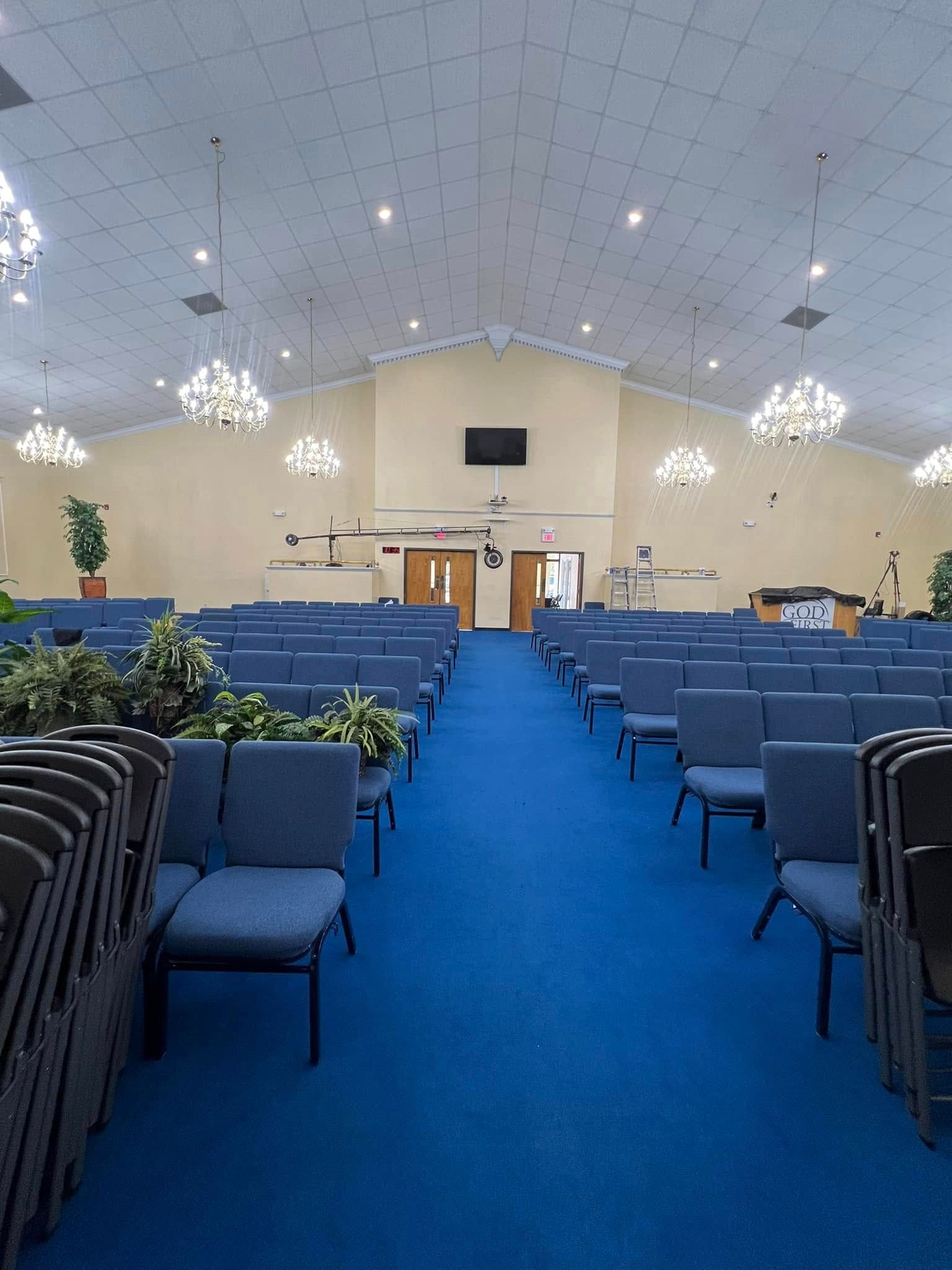 A church sanctuary with rows of blue chairs on both sides of a central aisle leading to a stage with wooden doors.