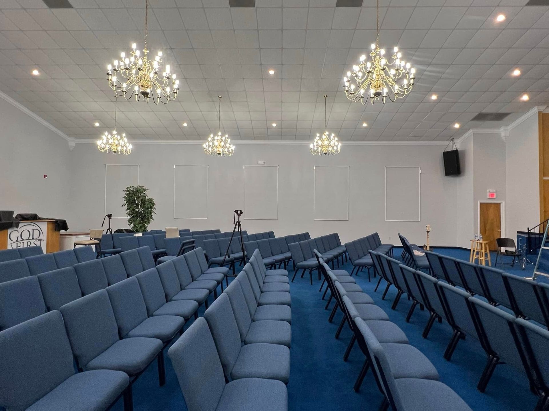 Rows of blue chairs arranged in a worship space with multiple chandeliers hanging from the ceiling.