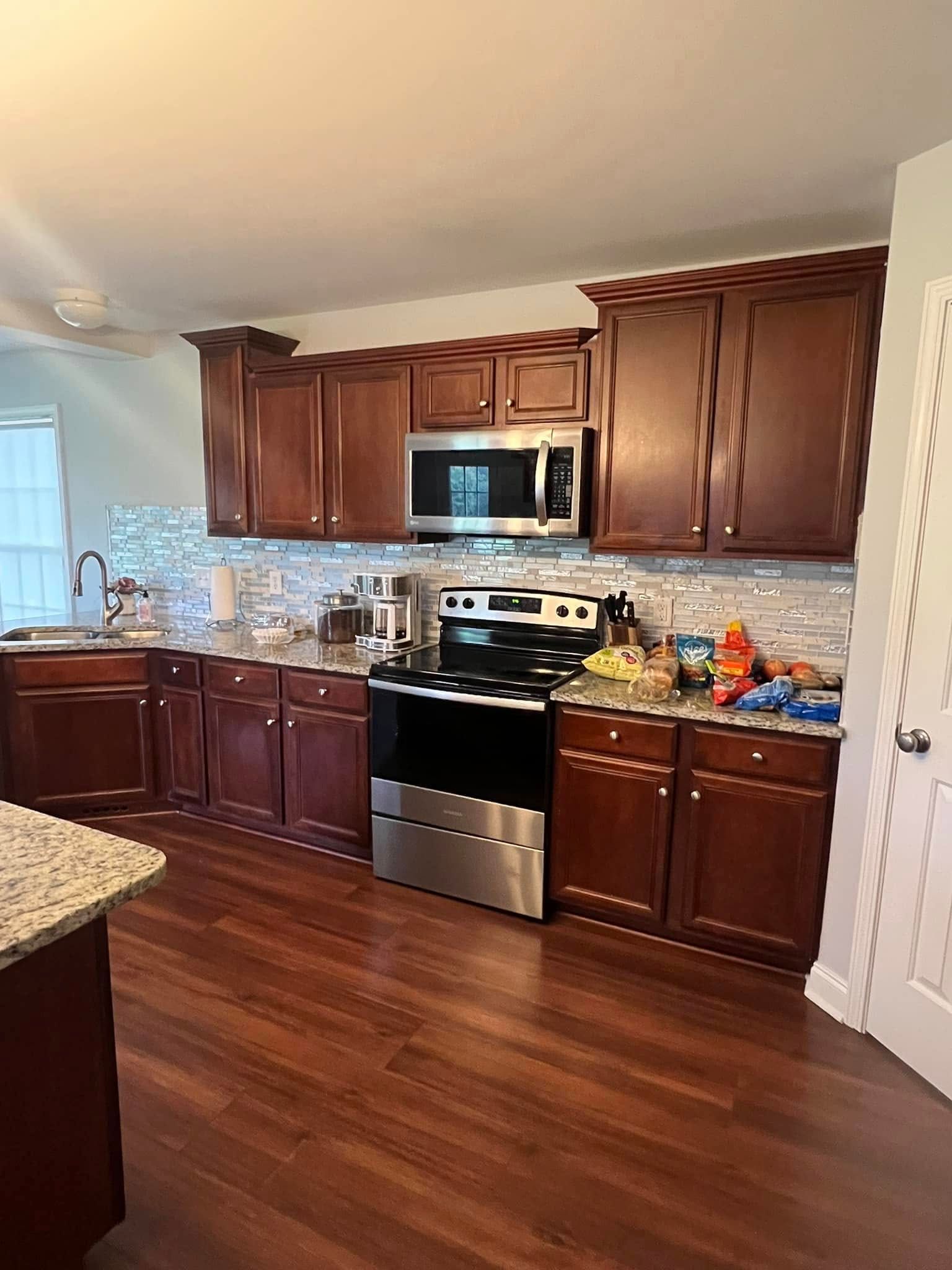 A modern kitchen with dark wood cabinets, stainless steel appliances, speckled countertops, and a light-tiled backsplash.