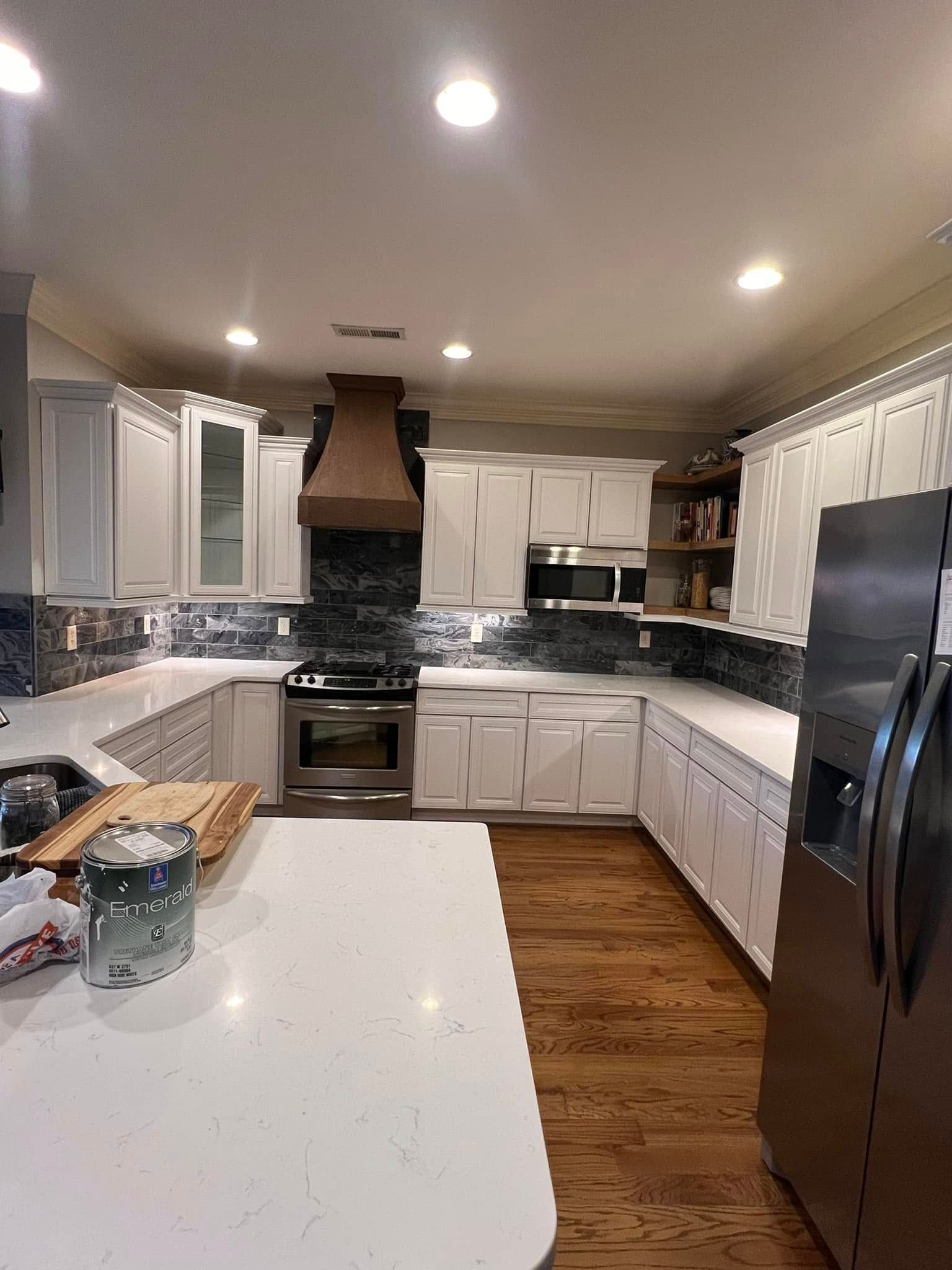 A kitchen featuring white cabinets, a dark wood range hood, a marble-patterned backsplash, and a large white island.
