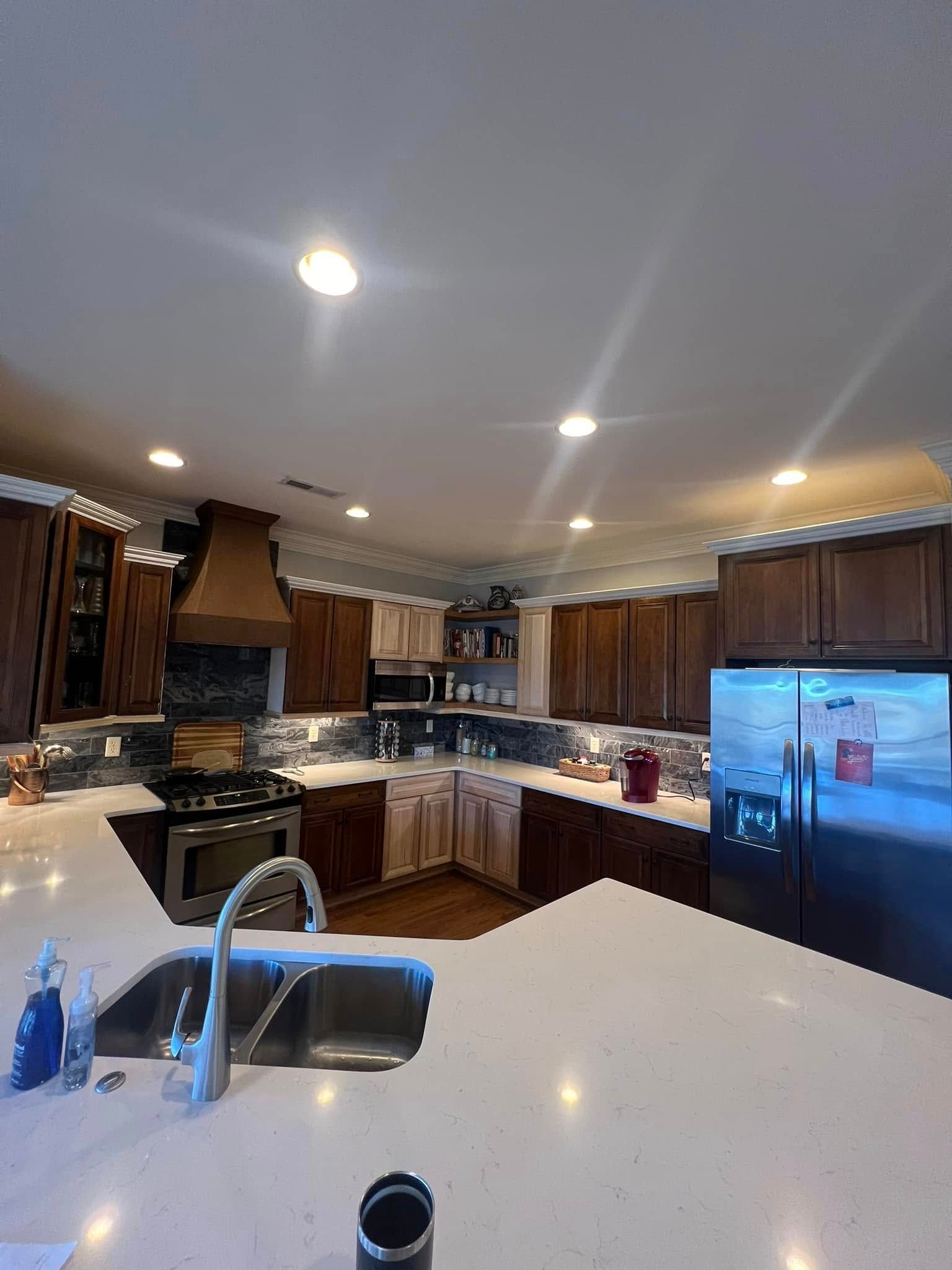 A spacious kitchen with dark wood cabinets, white countertops, stainless steel appliances, and recessed lighting.