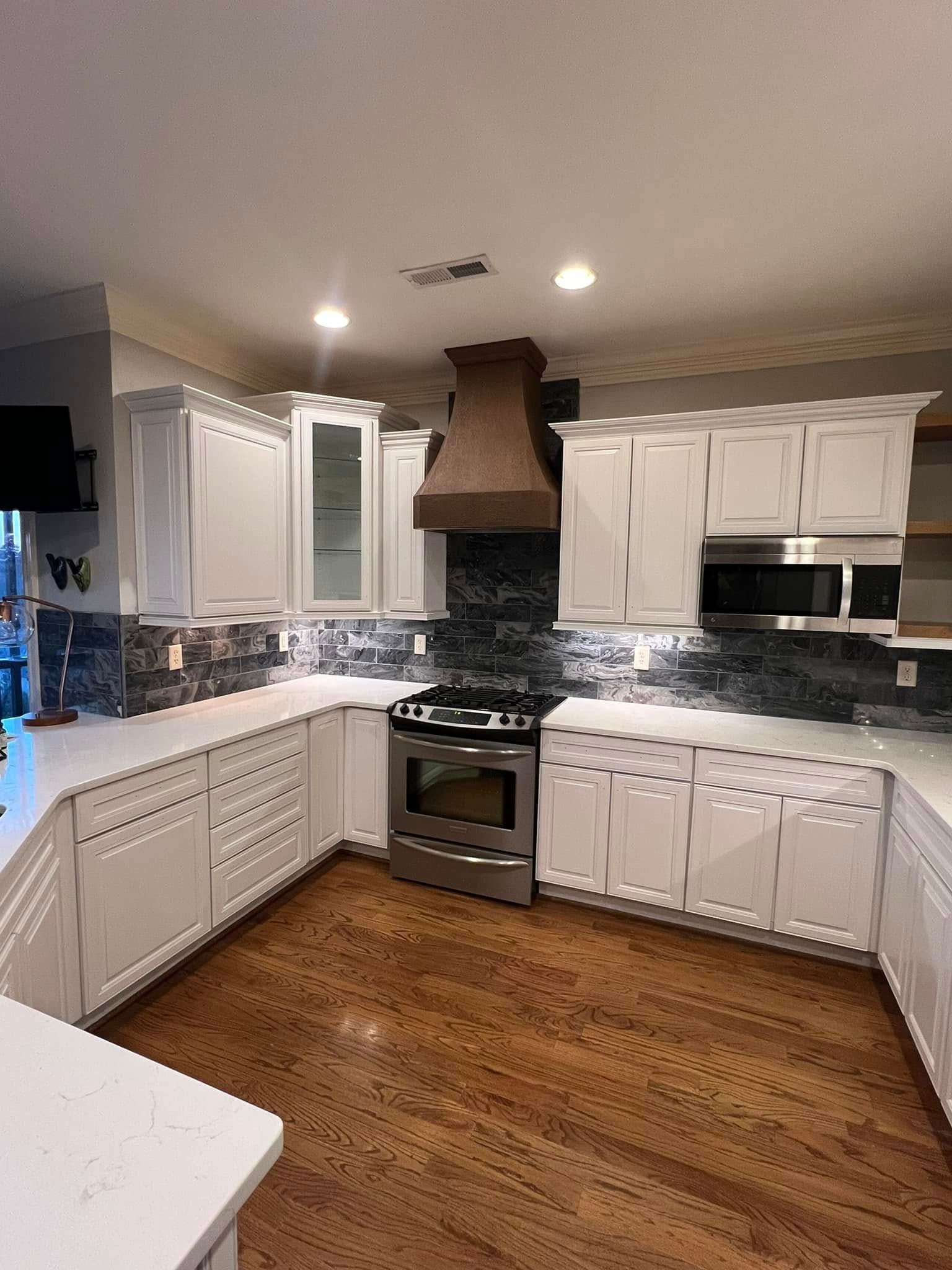 A U-shaped kitchen with white cabinets, light countertops, dark stone backsplash, stainless appliances, and wood floors.