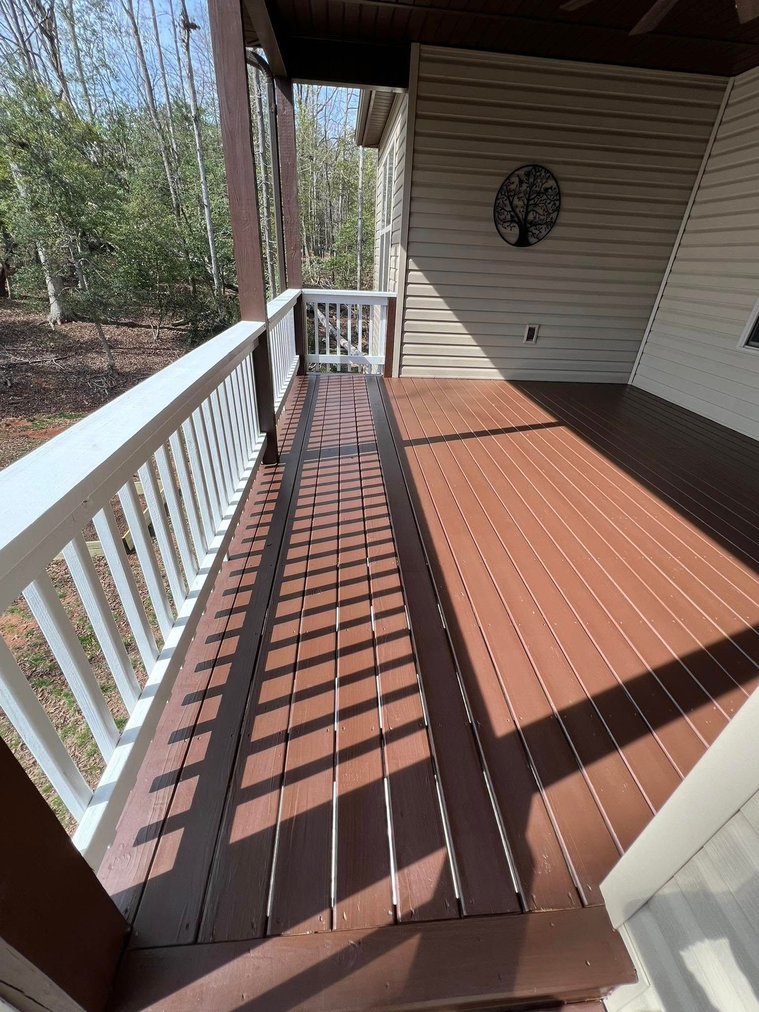A wooden deck with a white railing and patterned shadows cast by a roof overhang, viewed from an open doorway.