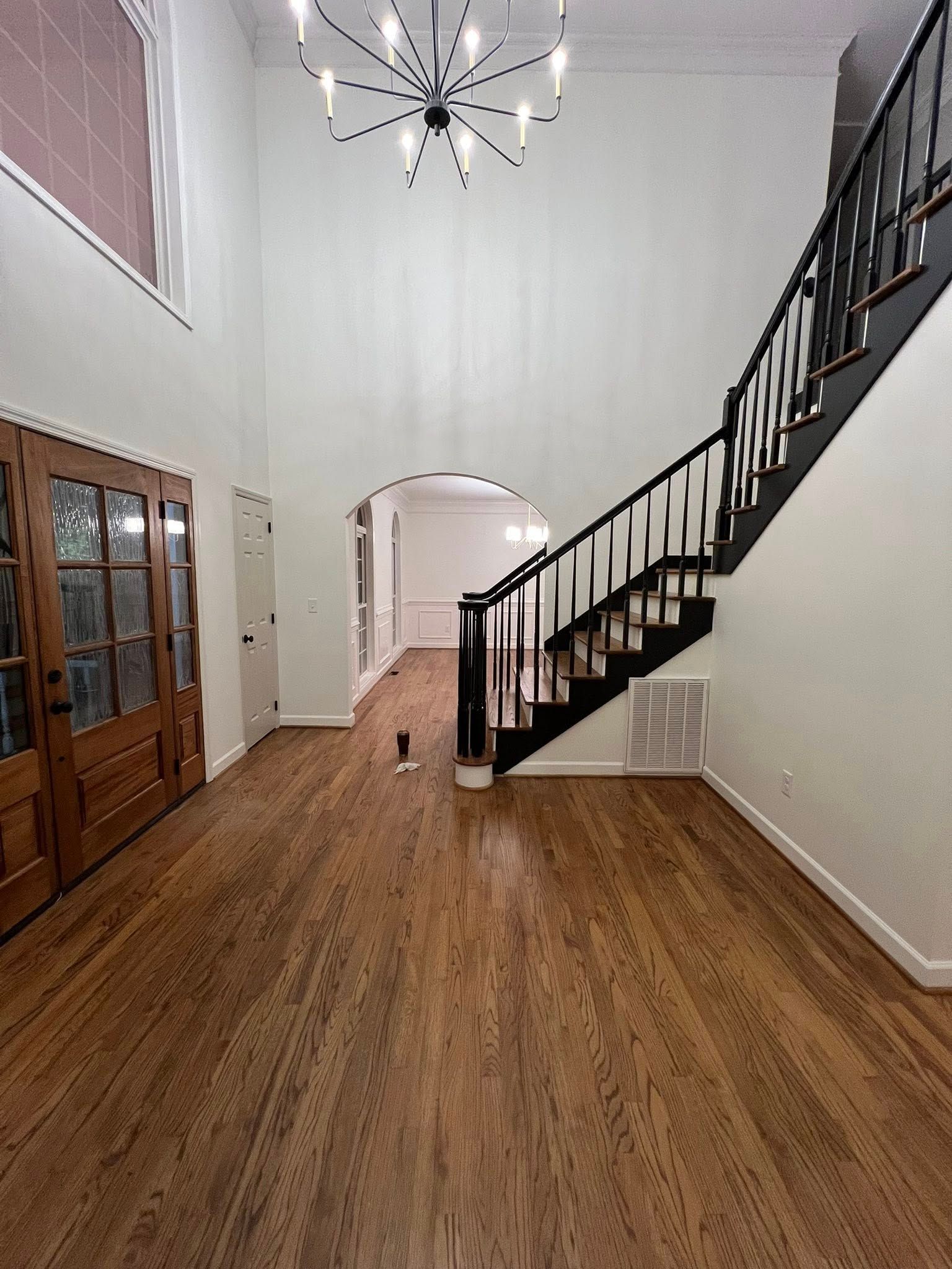 Foyer with wood floors, a grand staircase with dark railings, a crystal chandelier, and wooden double doors.