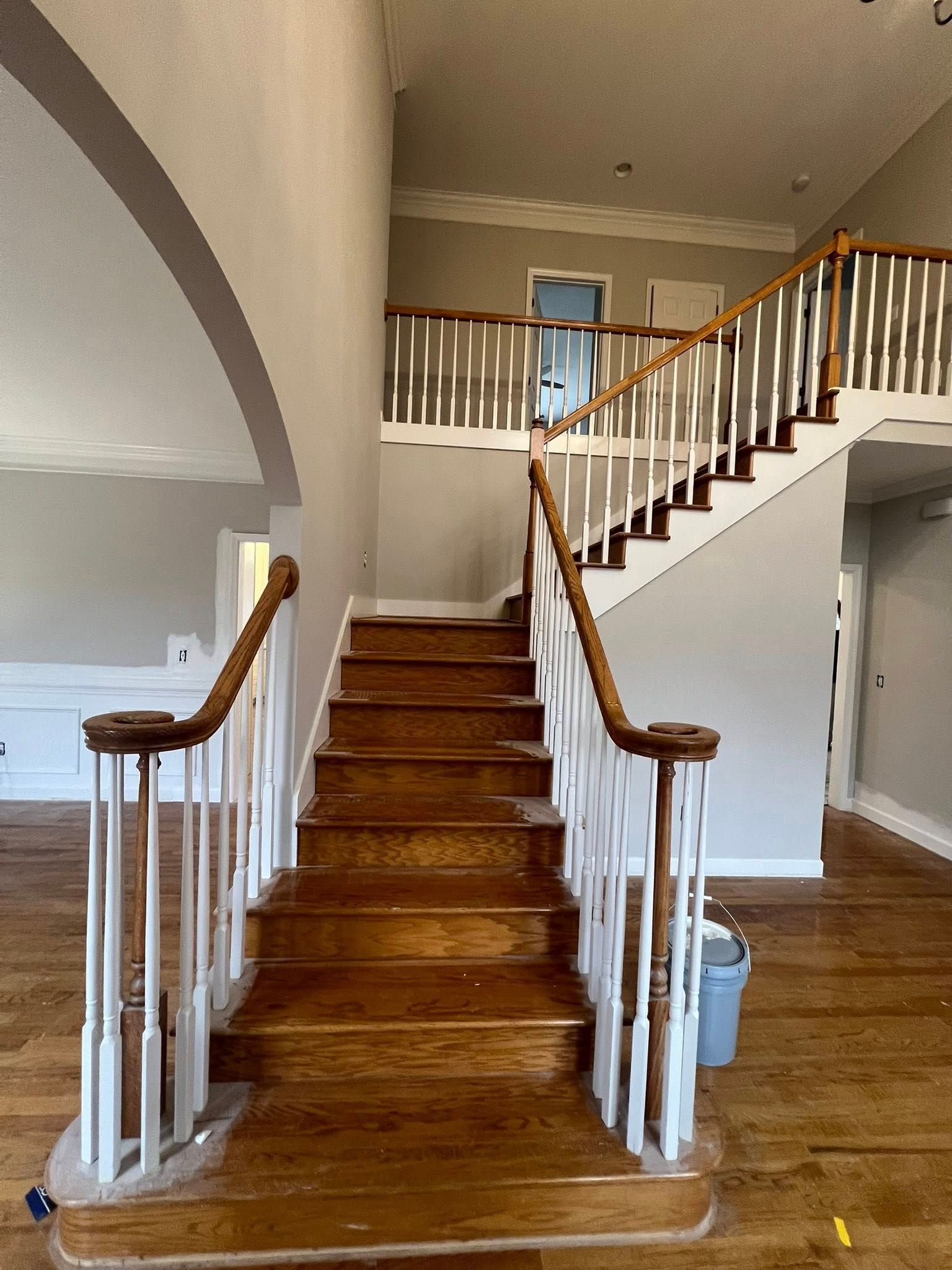 A wooden staircase with white spindles and a stained wood railing centered in a light gray foyer with hardwood floors.