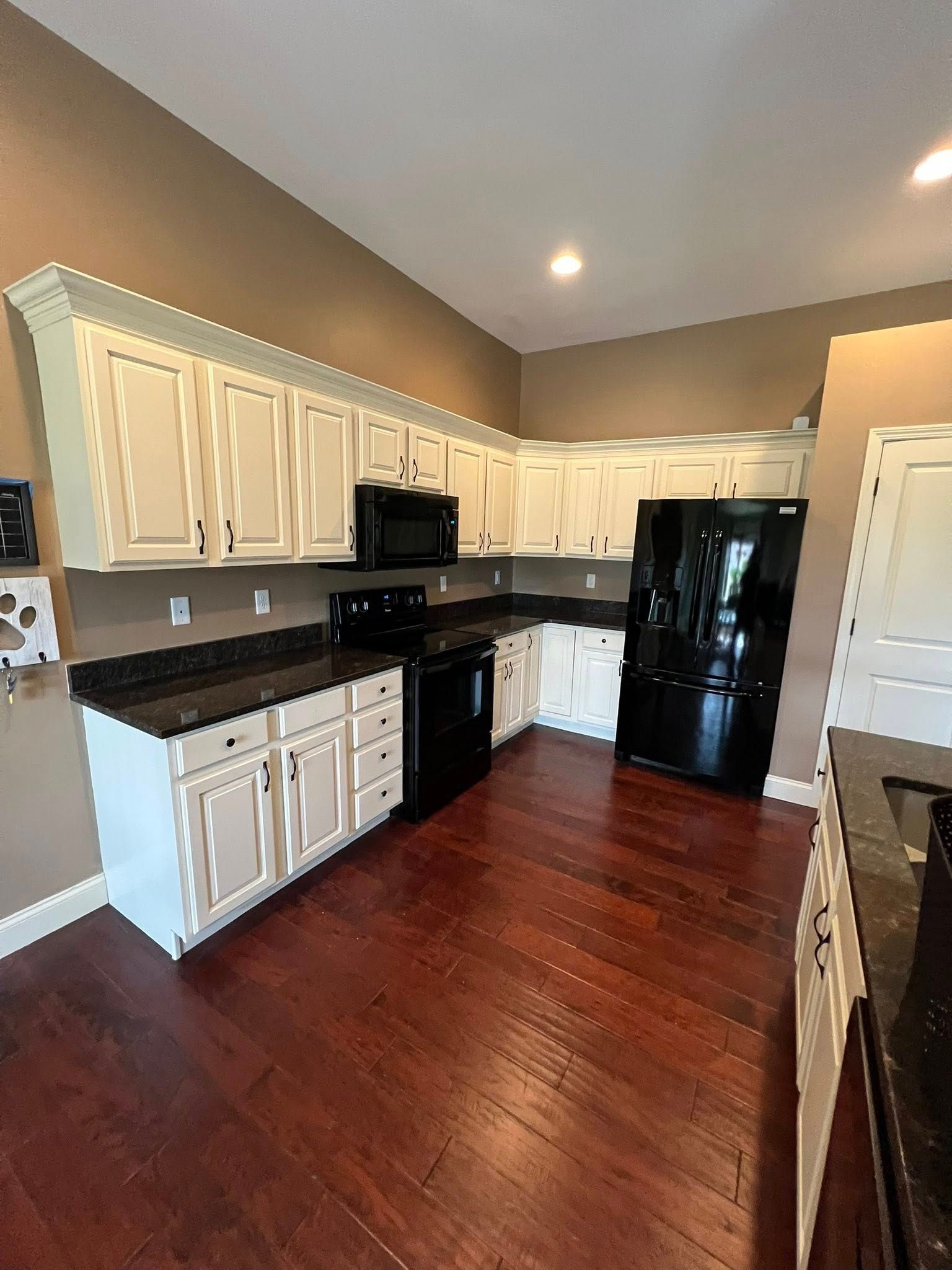 A kitchen featuring white cabinets, dark countertops, black appliances, and dark wood flooring.