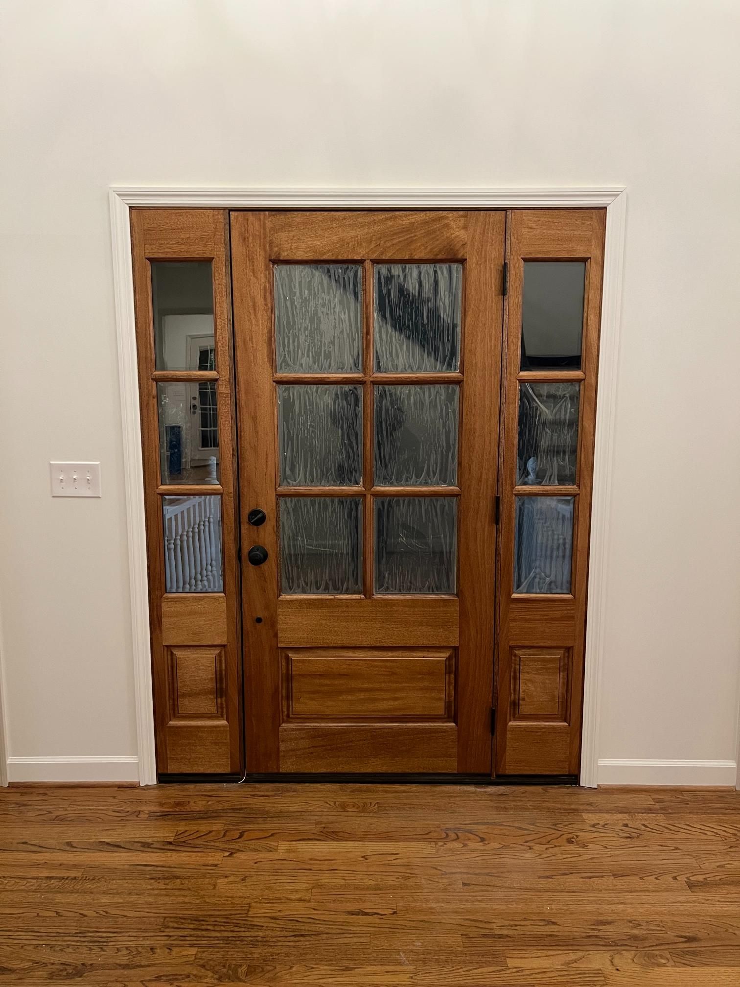A wooden front door with six glass panes and matching glass sidelights, set in a white wall above hardwood floors.