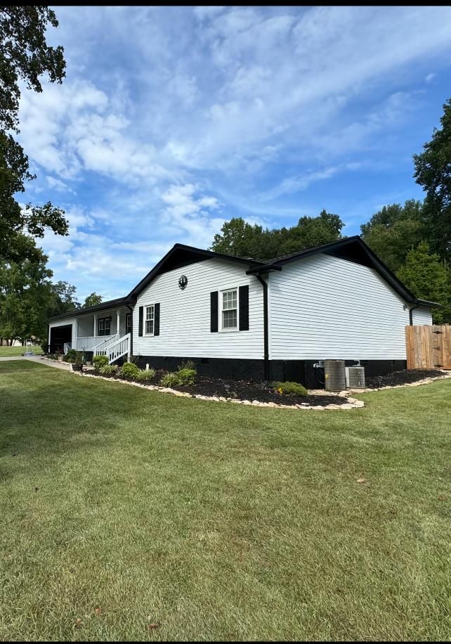 A white house with black trim and a dark foundation sits on a lawn against a blue sky with light clouds.