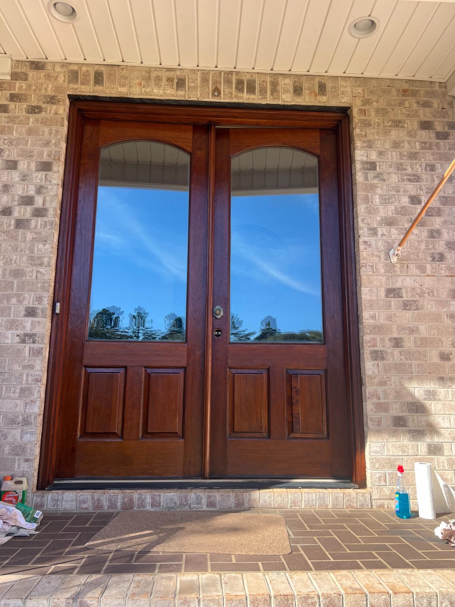 Double wooden entry doors with large glass panels, set in a brick exterior wall above a herringbone brick porch.