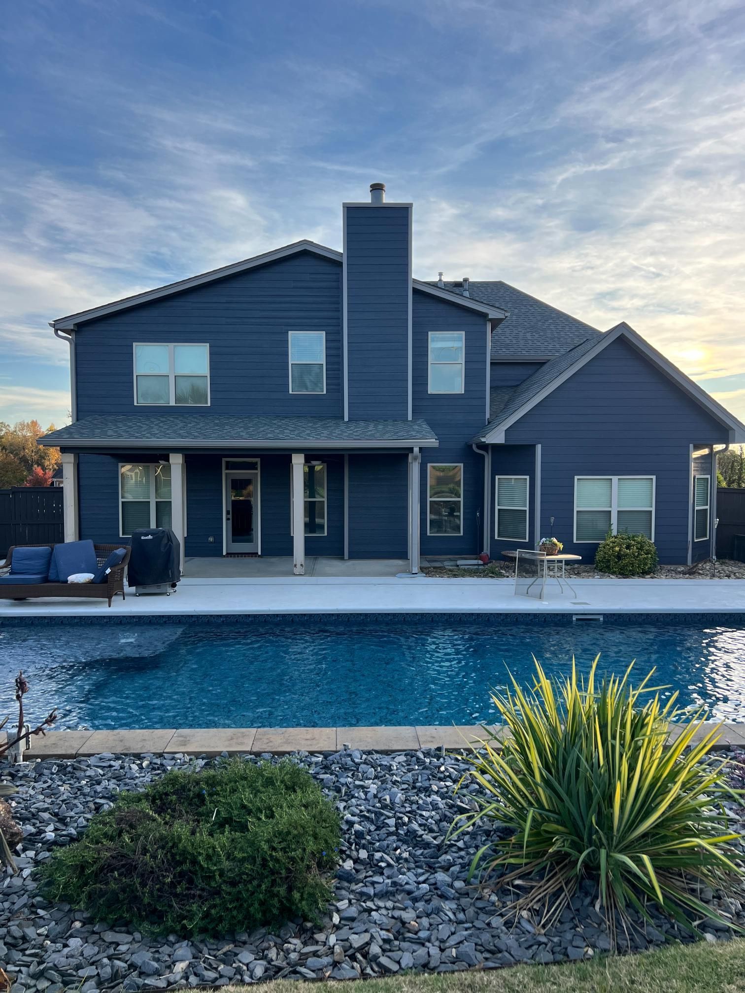 A two-story dark blue suburban house with a swimming pool in the backyard under a sunset sky.