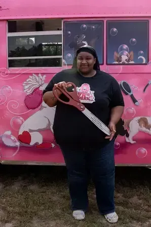 A woman is holding a pair of scissors in front of a pink bus.