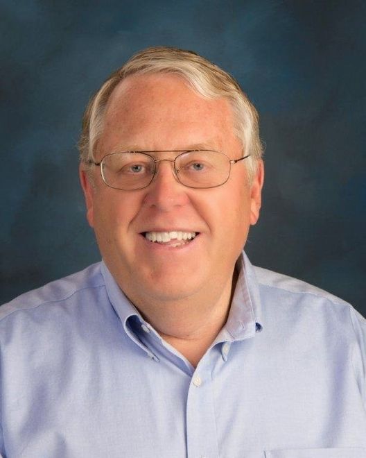 A man wearing glasses and a blue shirt smiles for the camera