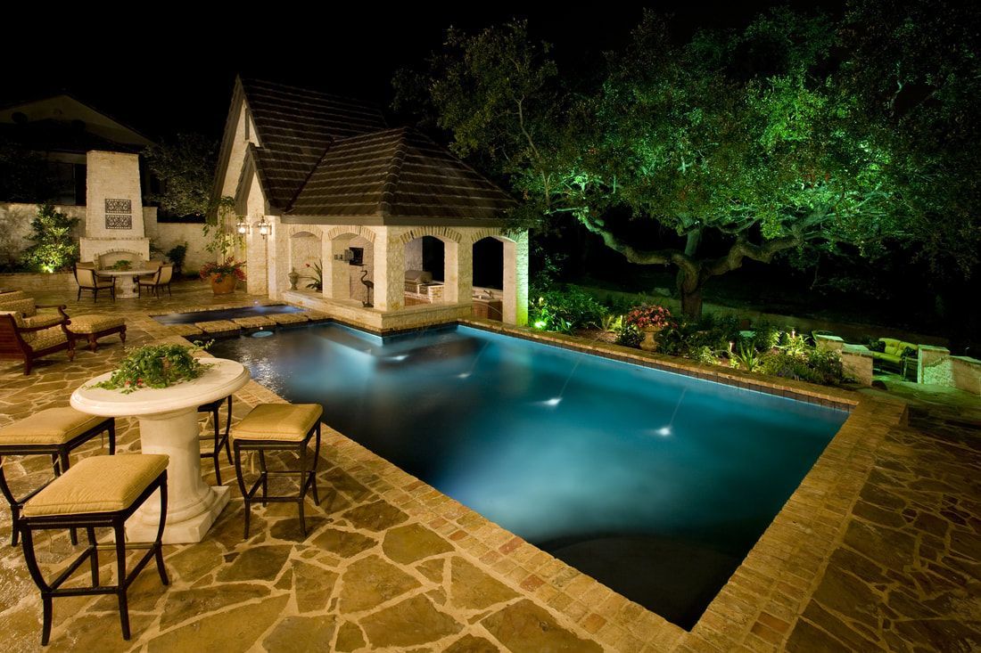 A large swimming pool is lit up at night with a gazebo in the background.