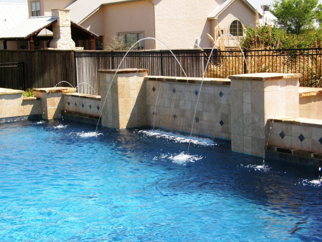 A swimming pool with a fountain and a house in the background
