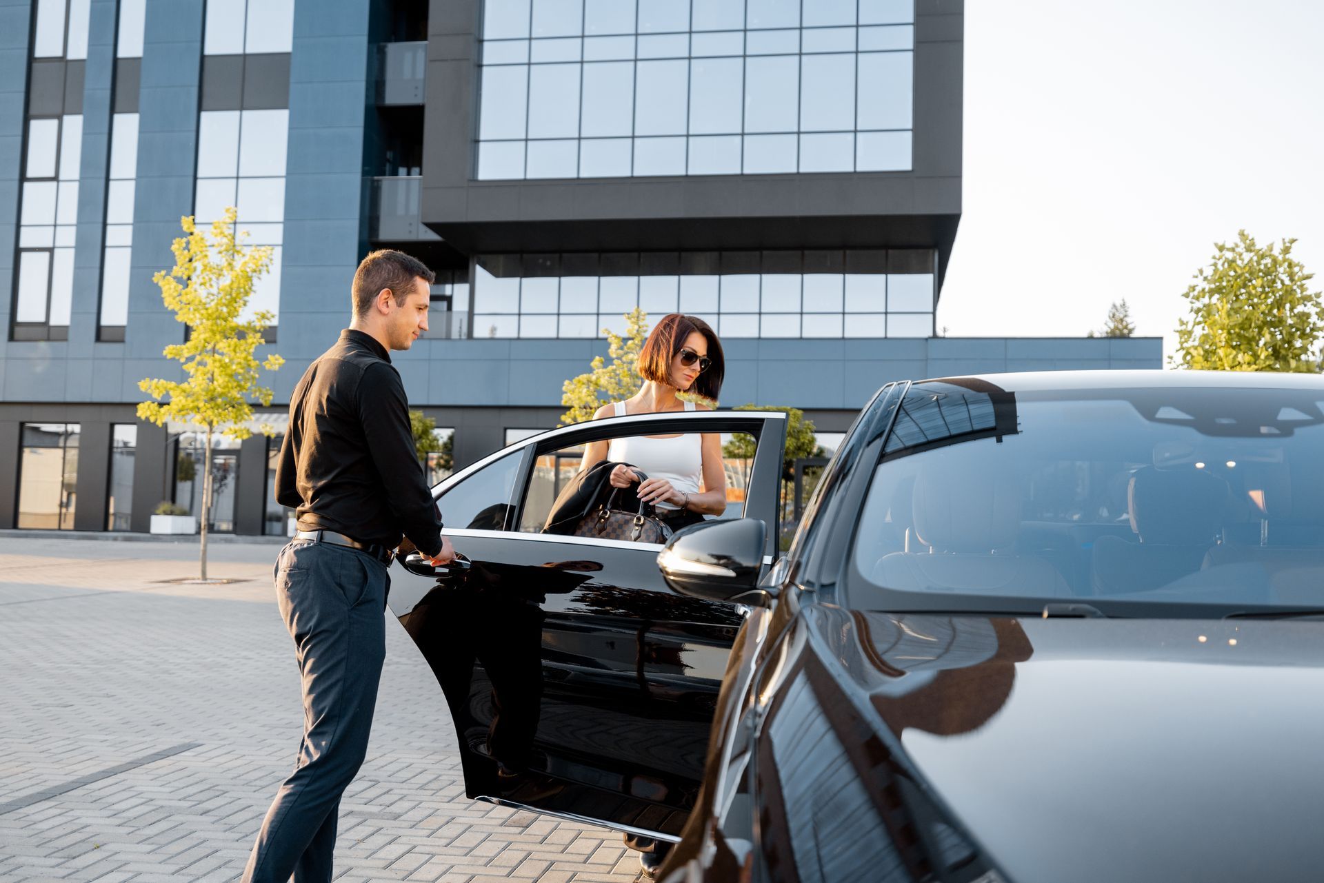 A man opening a car door for a woman in front of a modern building.