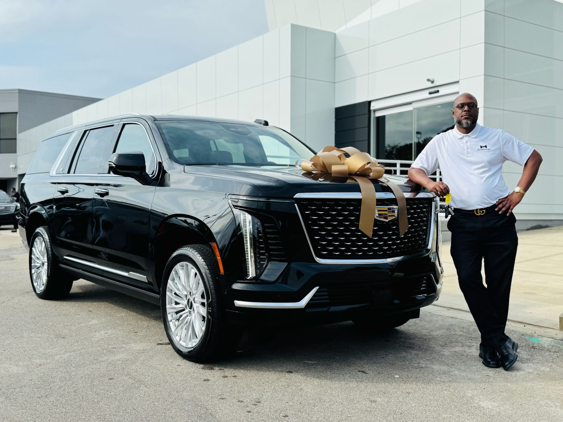 Man in front of a black SUV with a bow. He is in a car dealership.