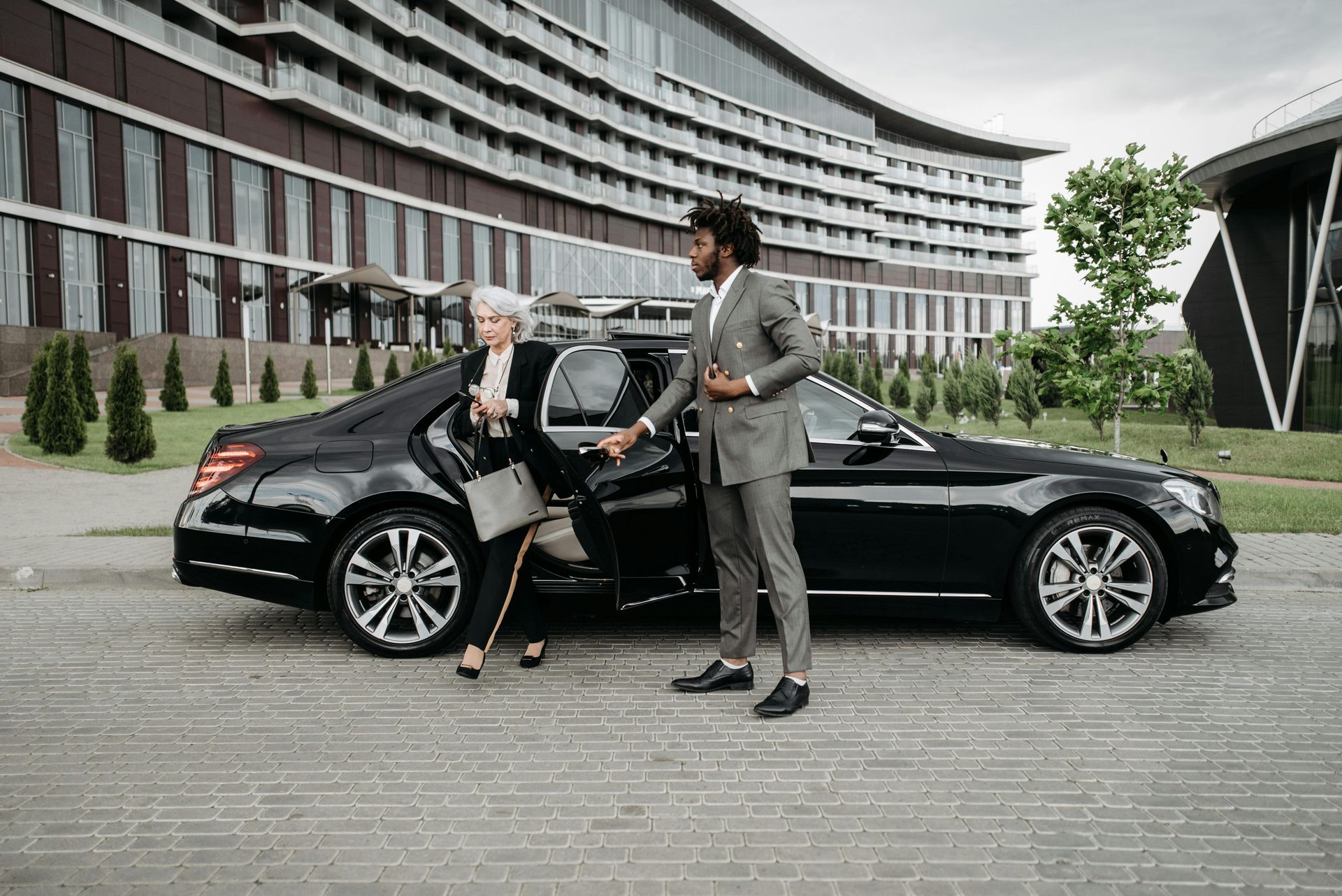 Professional chauffeur opening luxury black sedan door for businesswoman at upscale Memphis hotel