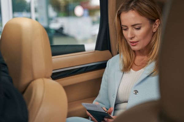 Woman in a car, looking down at a phone or wallet. Wearing a blue blazer, beige interior.